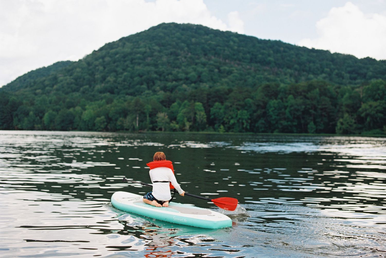 Someone paddleboarding on a serene lake with mountain views in the background.