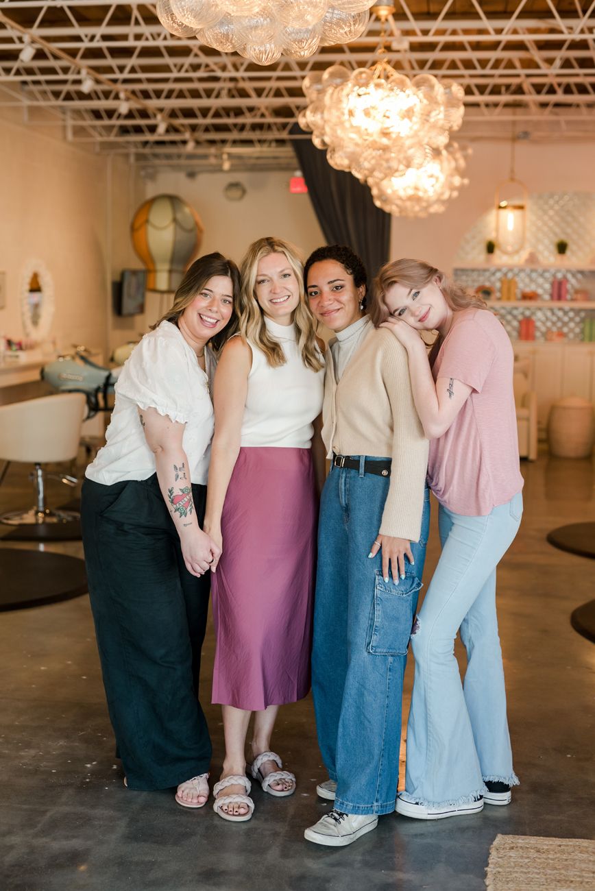 Group of four friends posing together in stylish retail space with chandelier lighting.