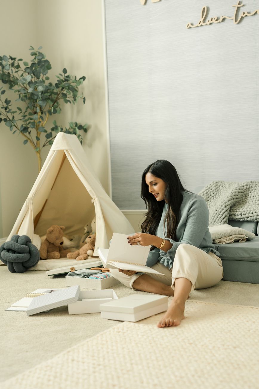 Person relaxing and reading in cozy tent setup with pillows and blankets.