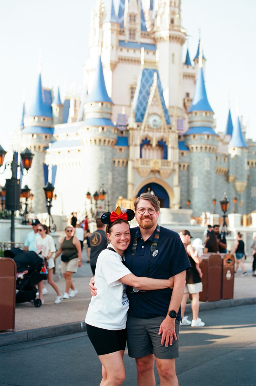 A pair of visitors sharing a hug in front of Cinderella Castle at Magic Kingdom.