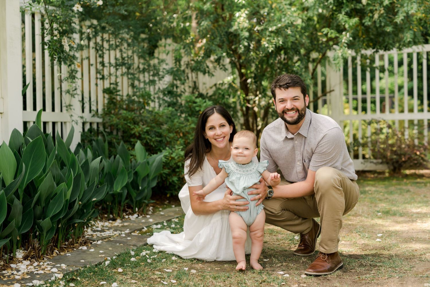 Family portrait in garden setting with white fence and lush greenery background.