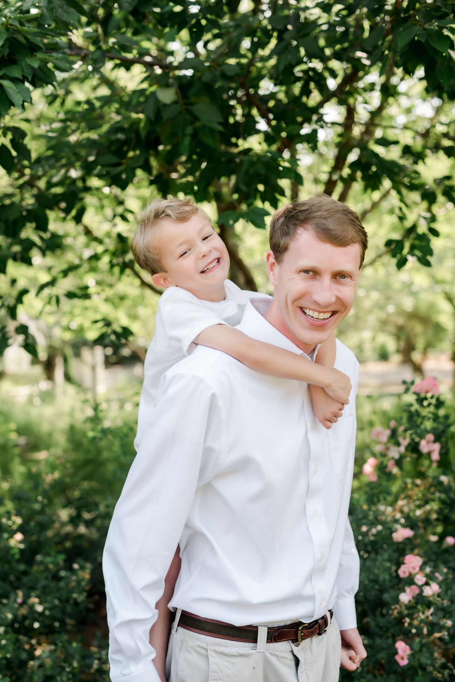 A playful piggyback ride moment captured against a leafy green garden backdrop.