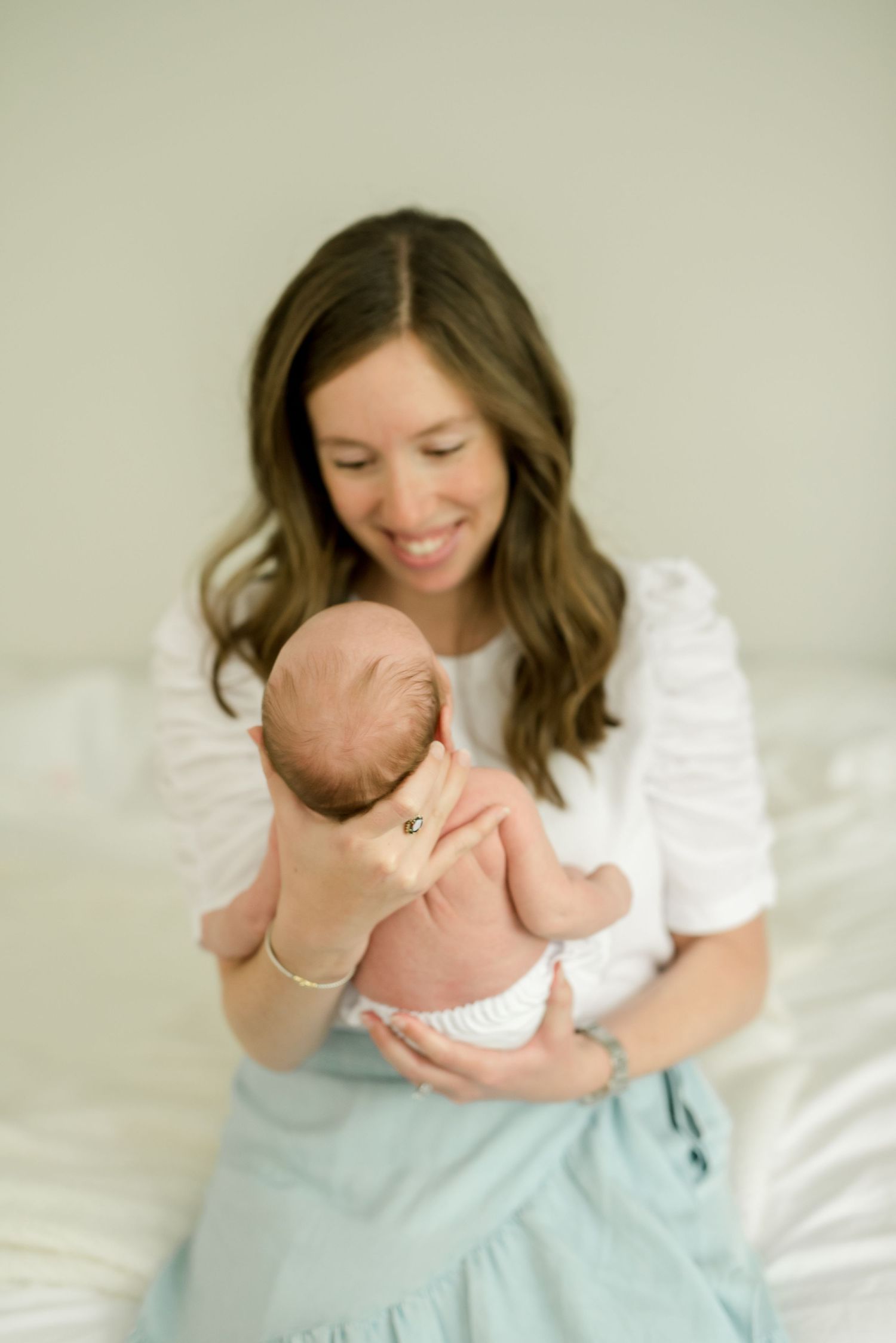 A joyful moment holding a newborn baby while sitting on white bedding.