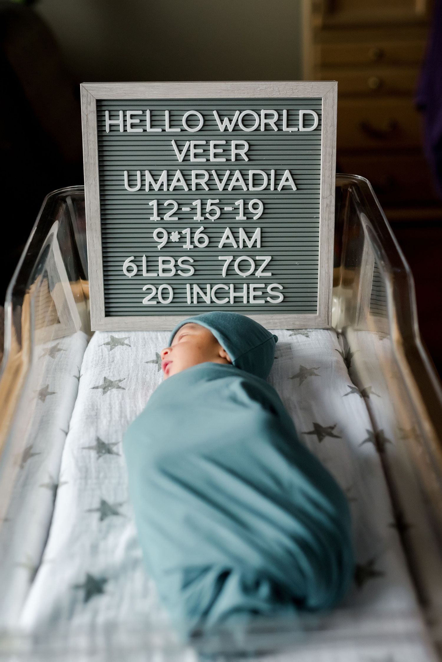 Newborn baby lies beneath birth announcement board showing weight, time and date details.