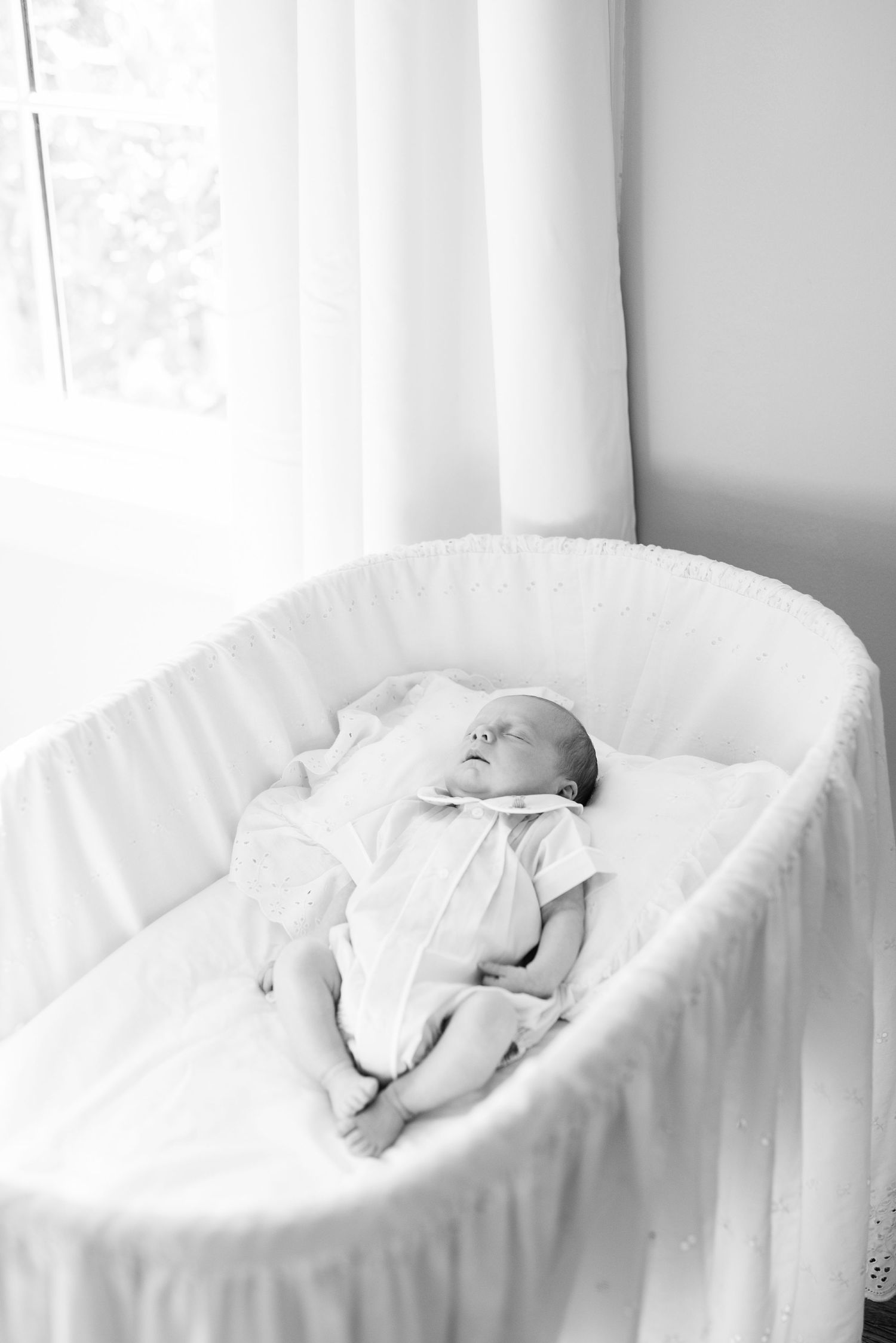 Peaceful black and white image of an infant sleeping in a white bassinet.