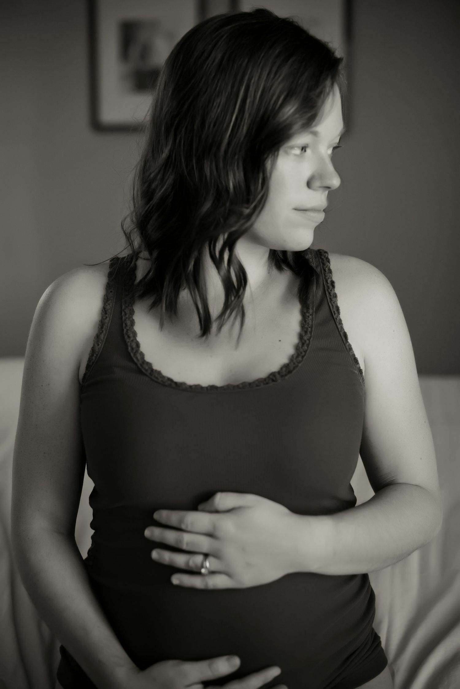 A side profile portrait of an expectant mother in a dark tank top against a simple background.