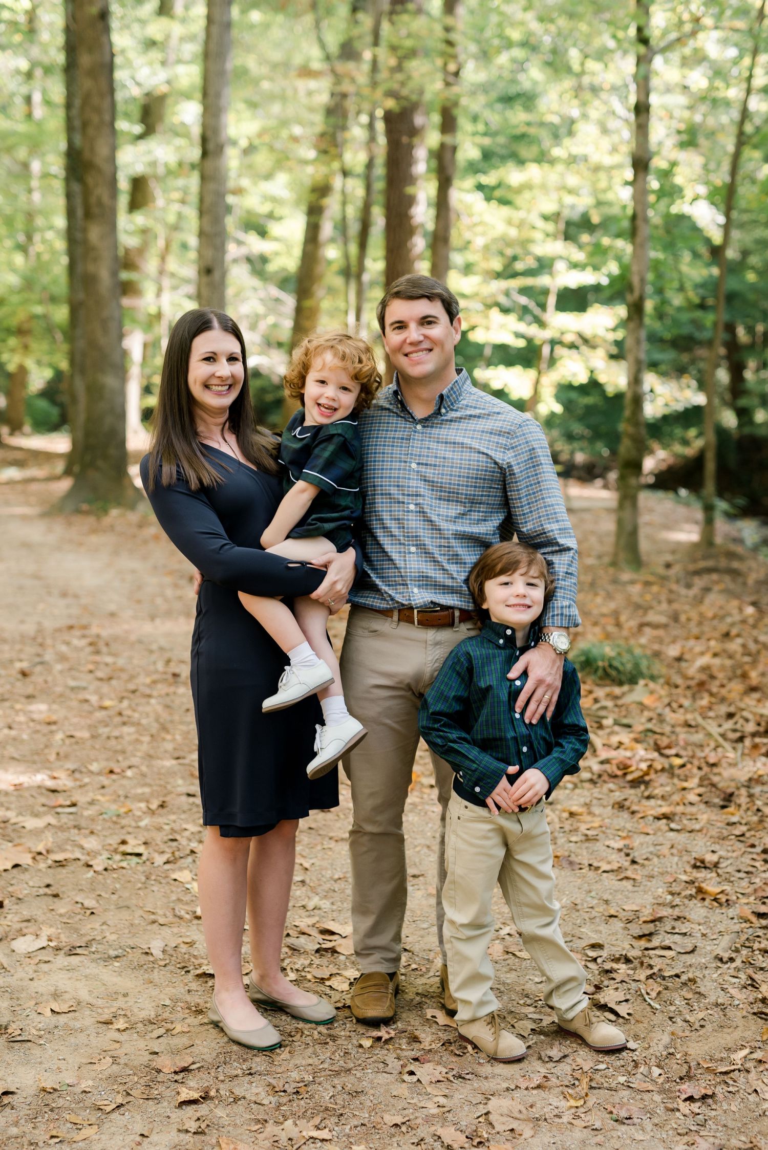 Family of four poses together on forest path wearing coordinated casual outfits.