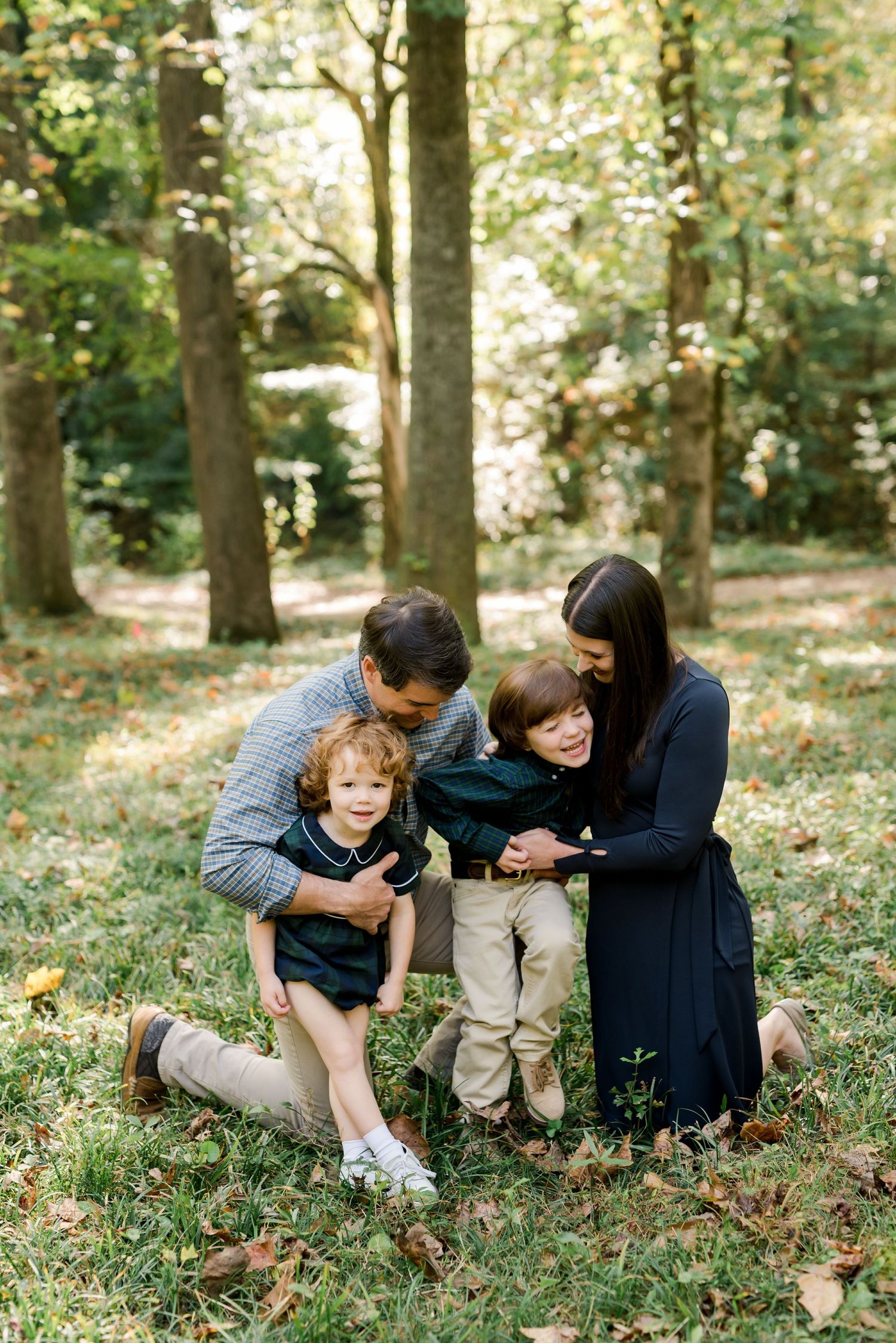 Family sharing a tender moment together while sitting on fallen leaves in a wooded setting.