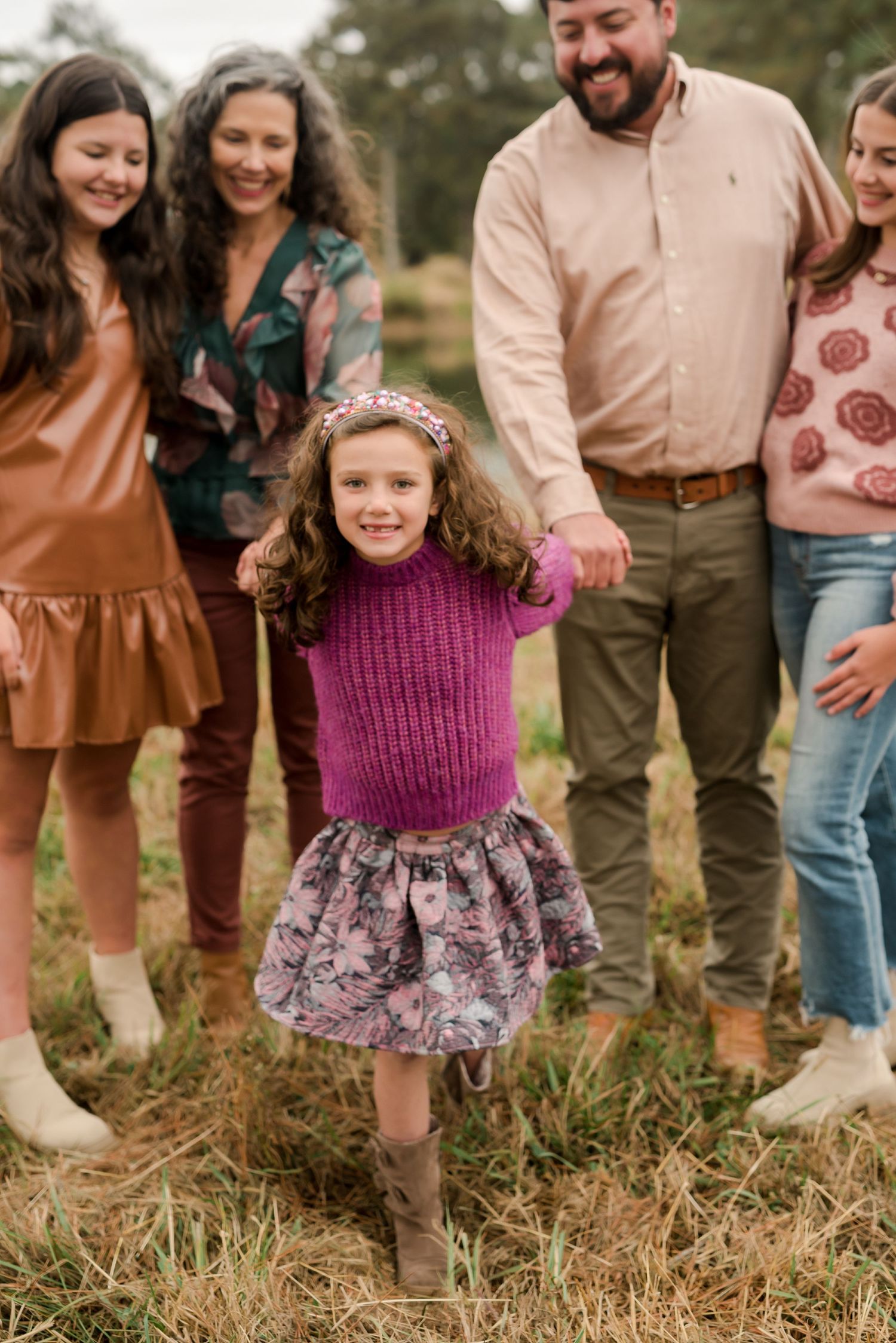 Family candid moment outdoors with person in purple sweater and floral skirt dancing.