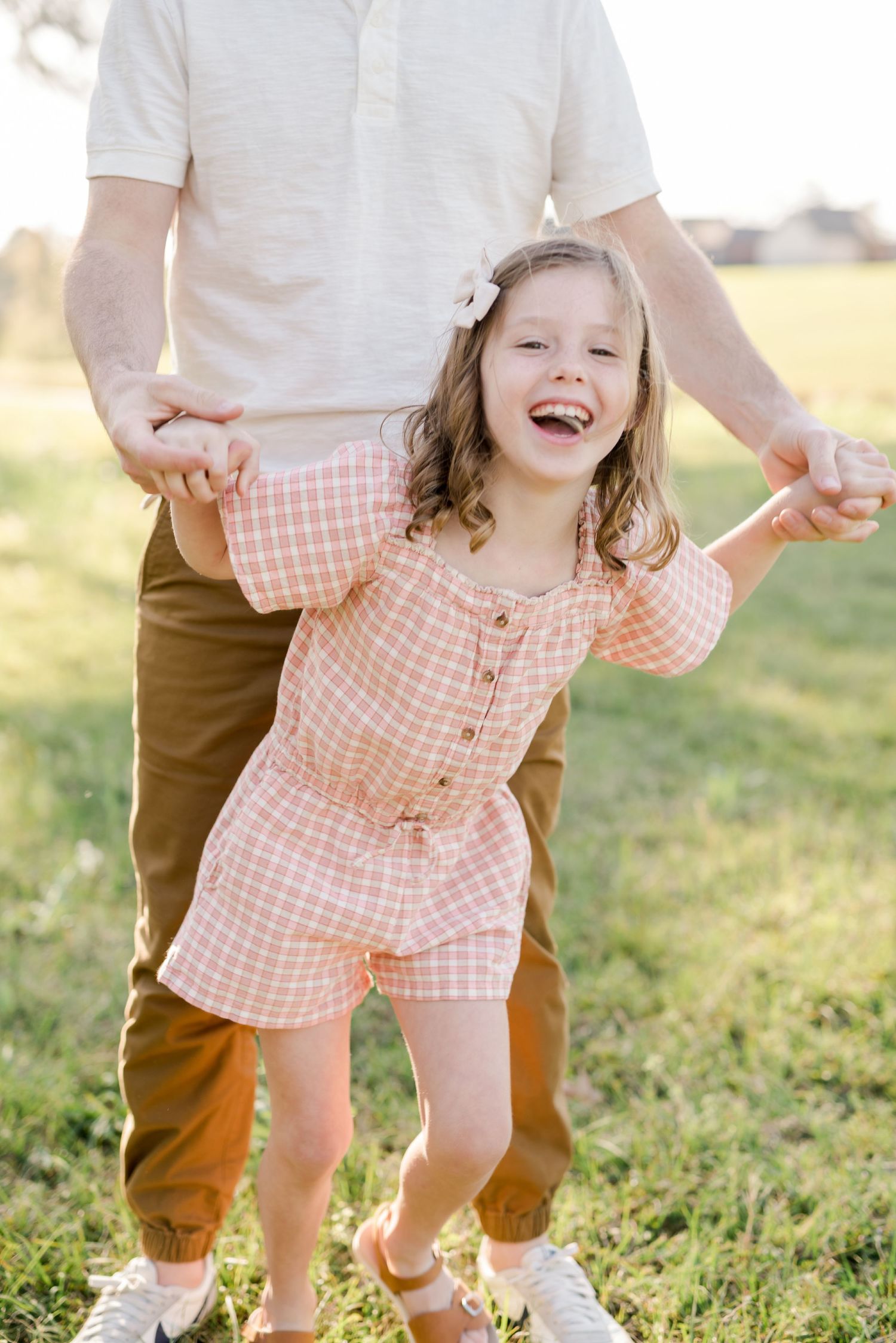 Playful outdoor moment capturing a child in a peach checkered outfit running in a sunny field.