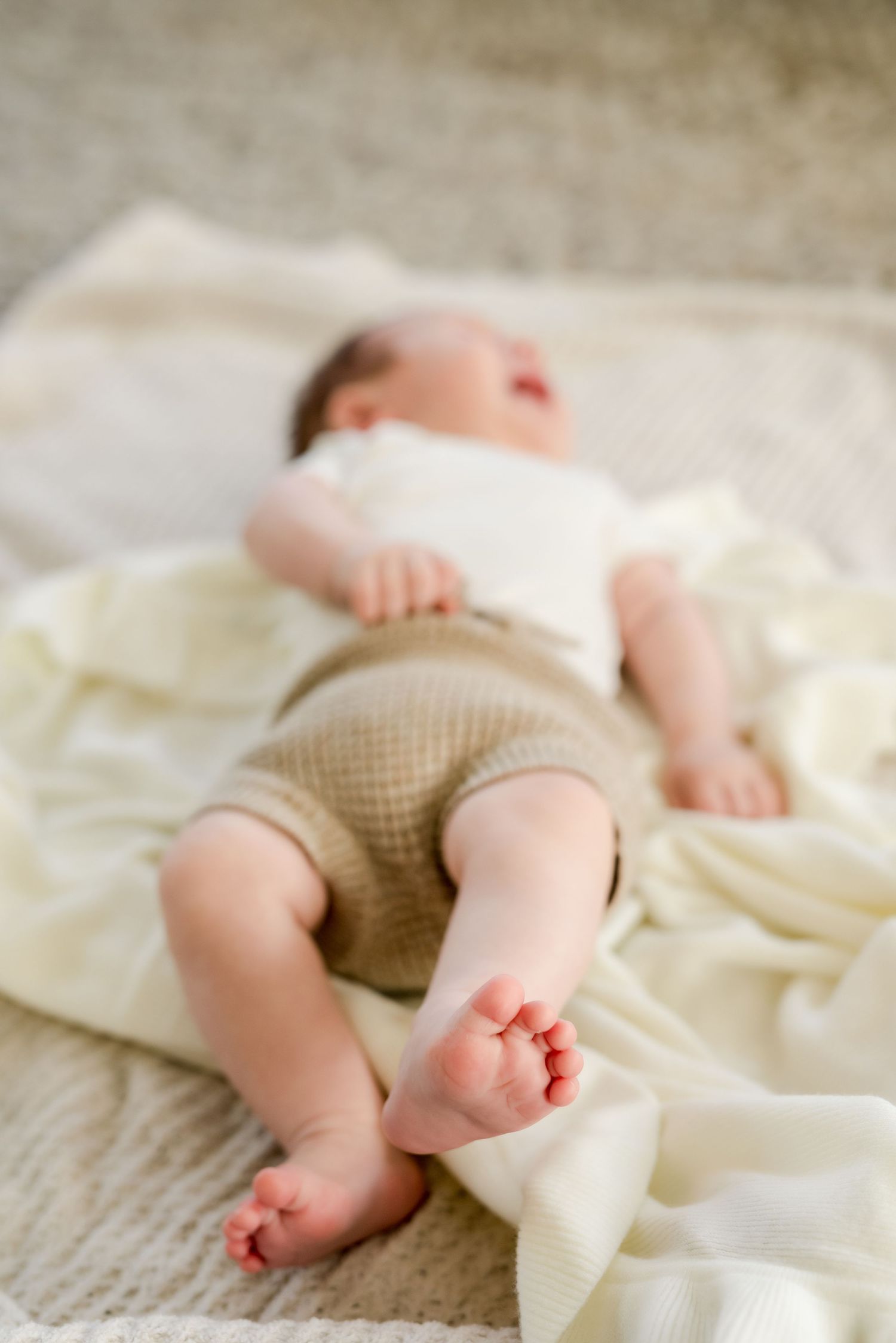 Baby sleeping peacefully on cream blanket wearing tan shorts.