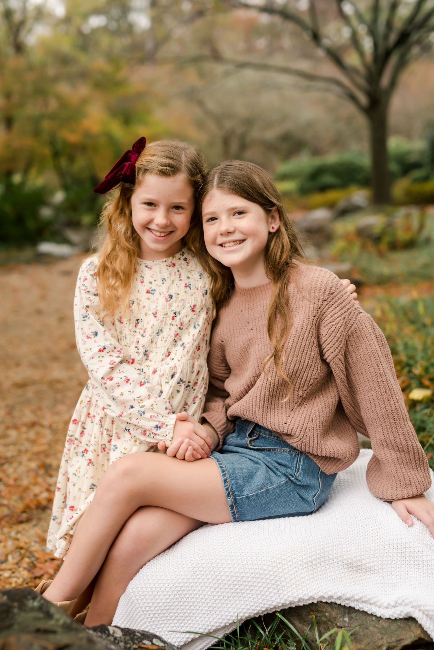 Two young people sitting outdoors in autumn wearing casual sweaters and dresses on a white blanket.