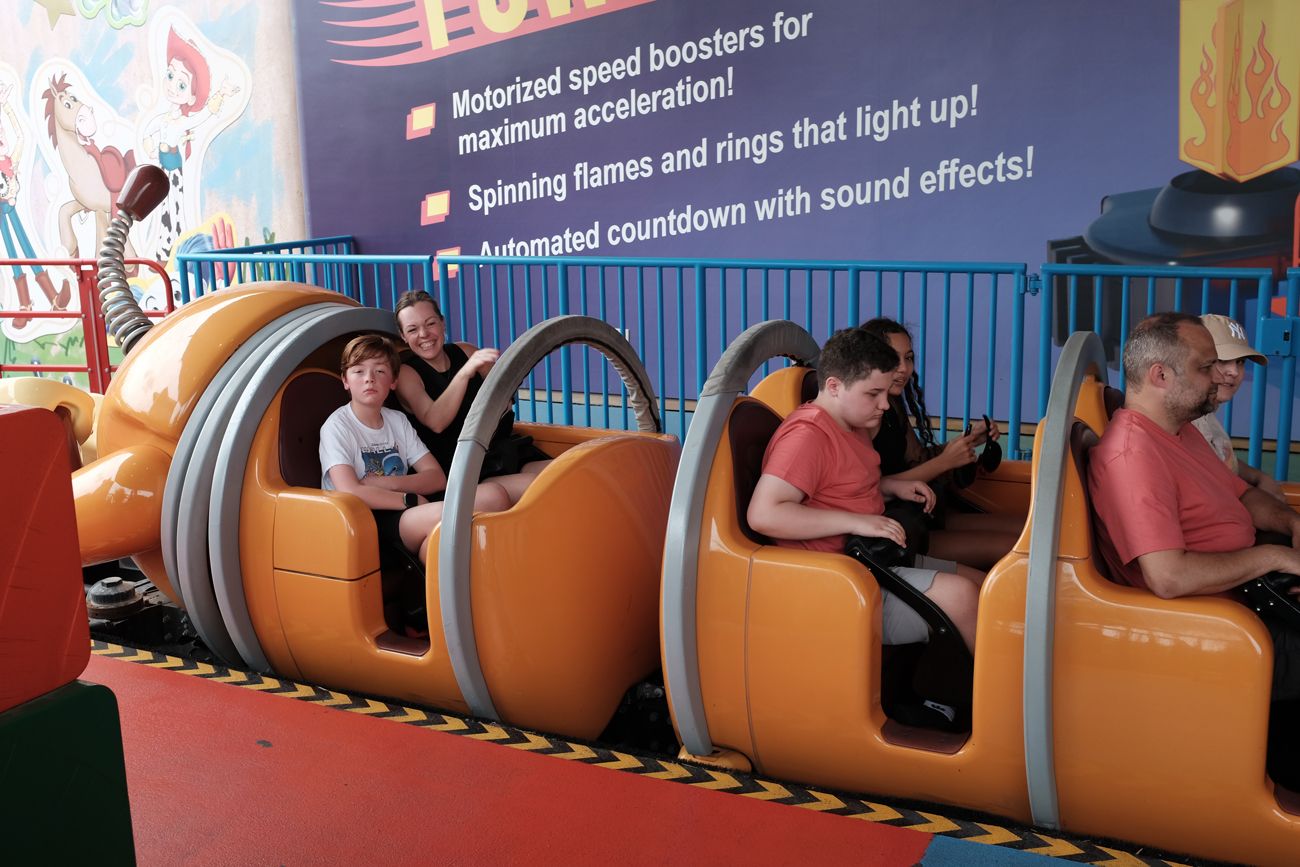 Visitors riding in orange segmented train cars on an indoor theme park attraction.