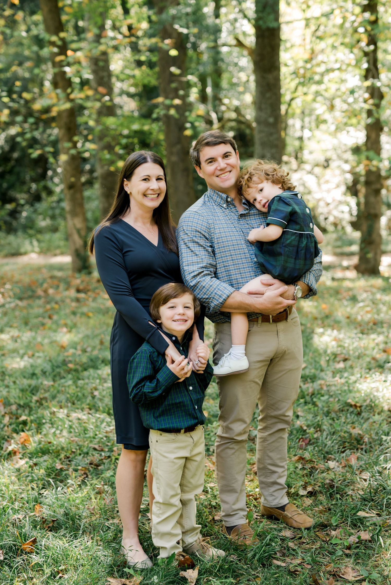 A family of four poses together for a portrait in a wooded setting during autumn.