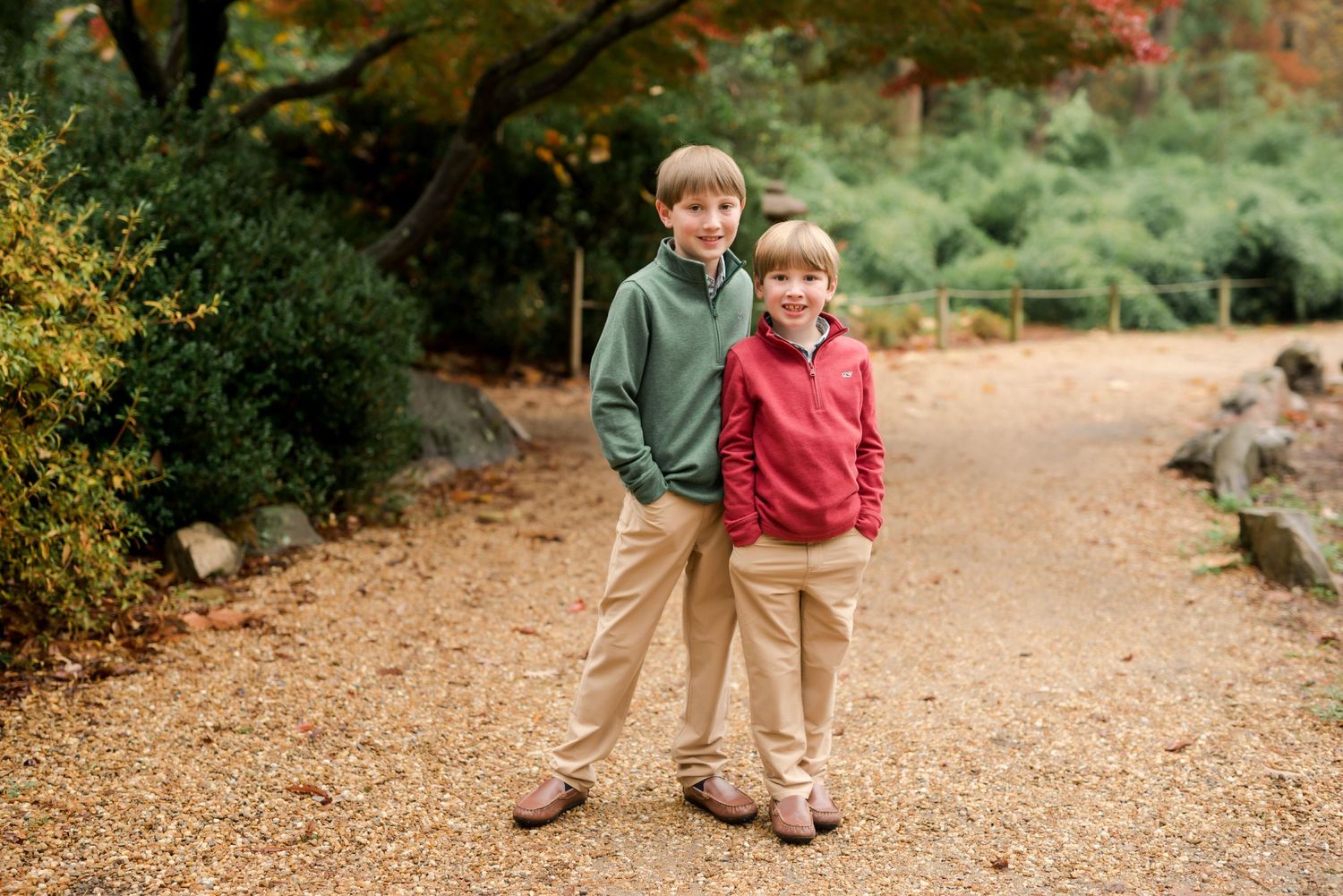 Two children in coordinated casual wear stand together on an autumn path.