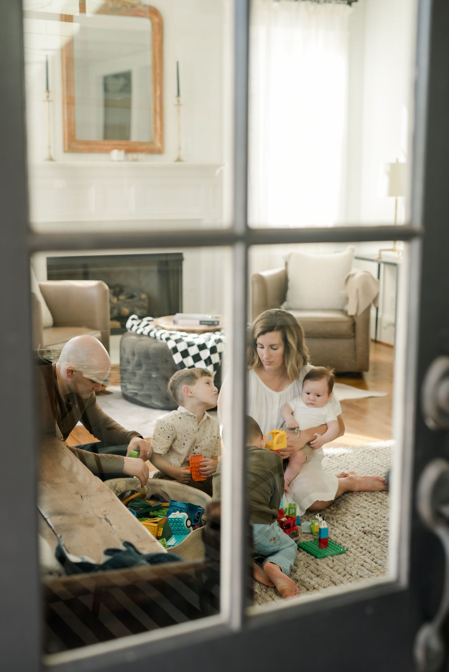View through window panes of family playing with toys on living room floor.