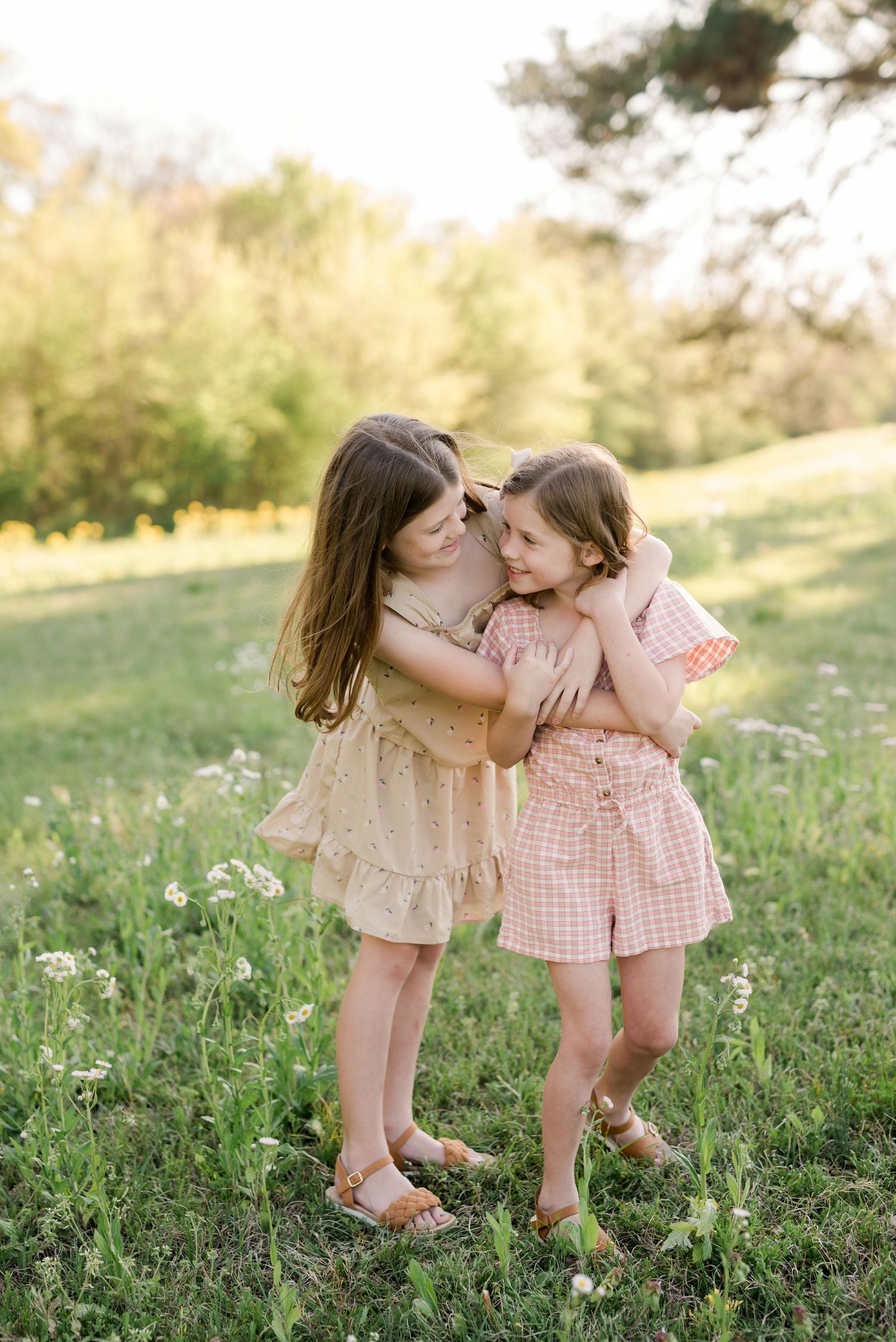 Two children in coordinating dresses share a sweet moment together in a wildflower field.