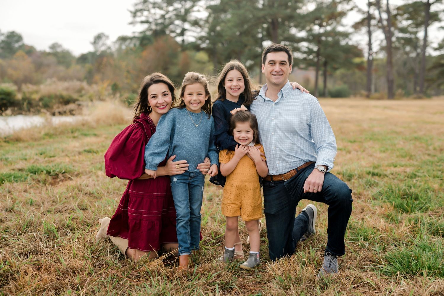 Family group poses together in coordinated outfits in an open field during fall season.
