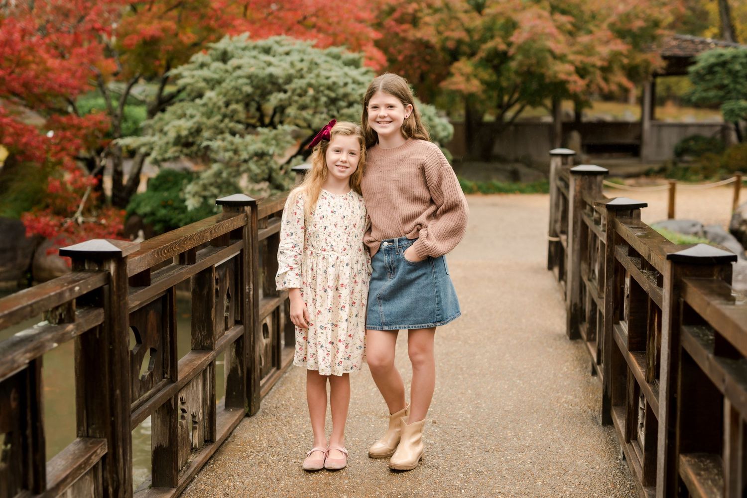 Two people holding hands while strolling across a wooden bridge surrounded by vibrant autumn foliage.