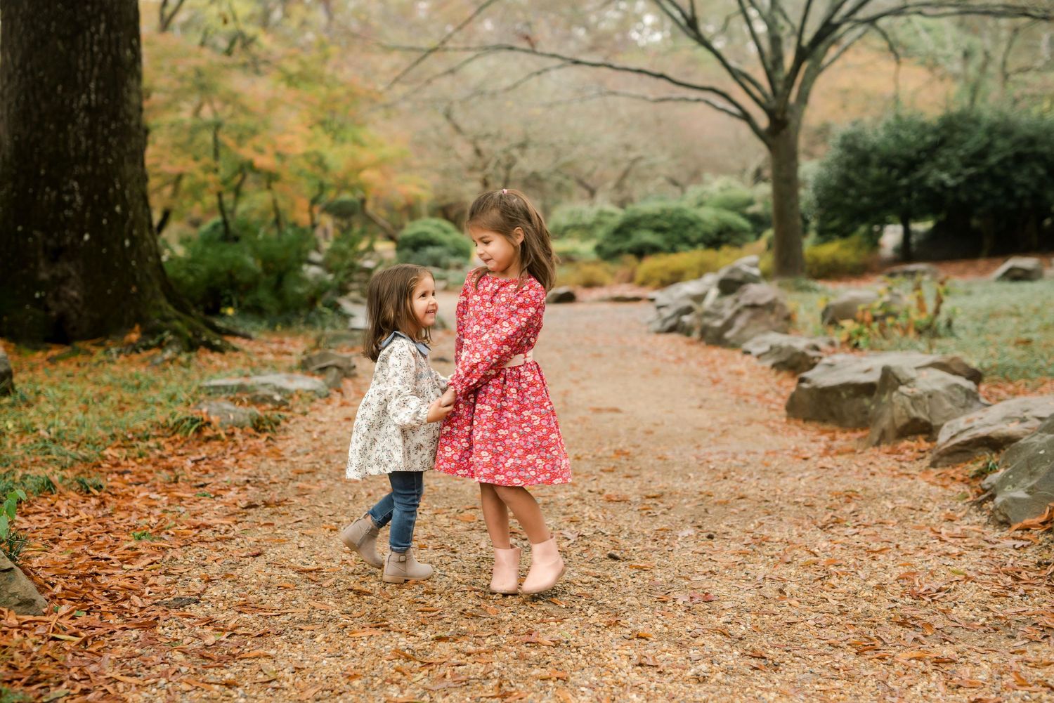 Two people in matching red dresses walking together on an autumn path covered in fallen leaves.