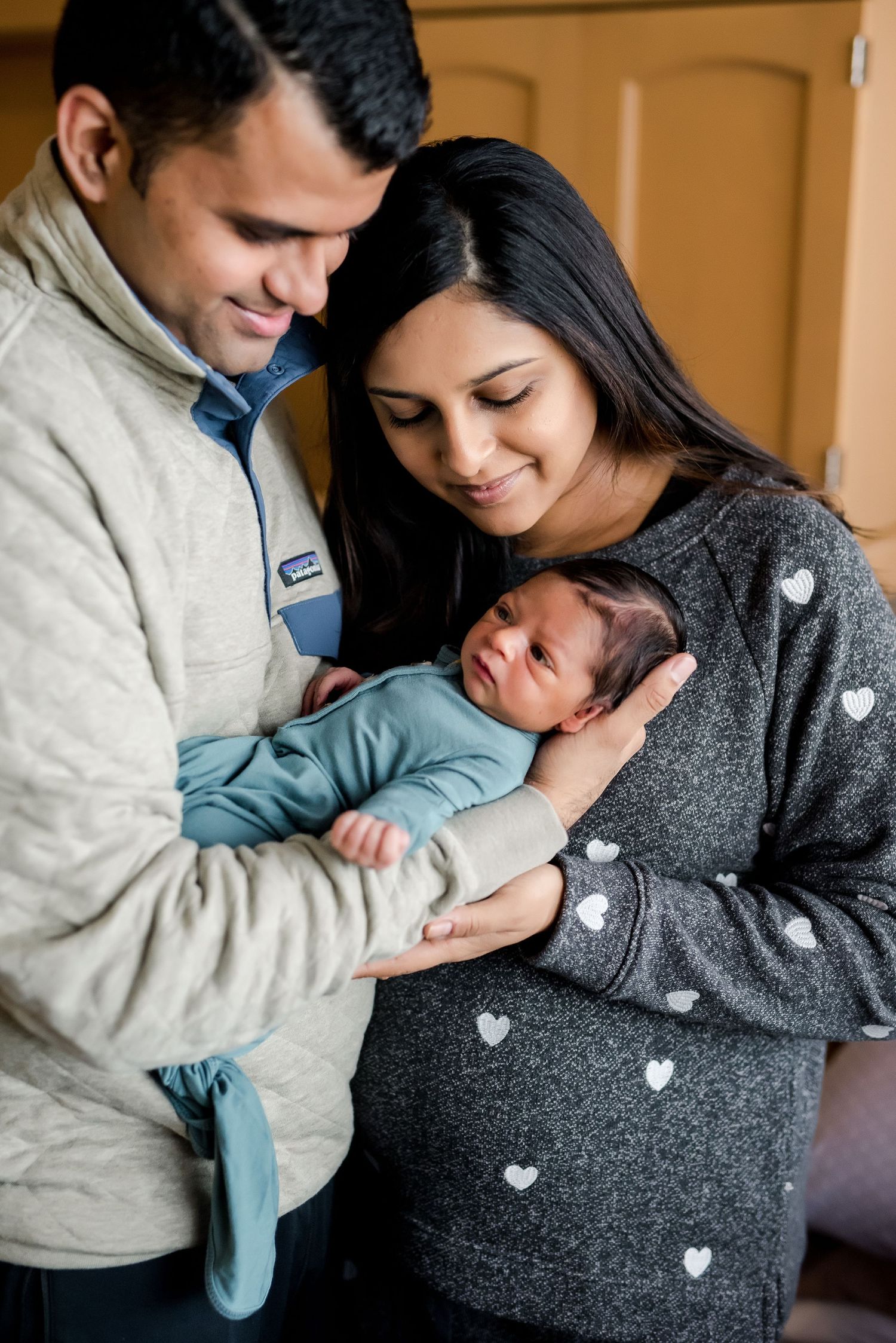 Parents share a tender moment with their newborn baby in a cozy indoor setting.