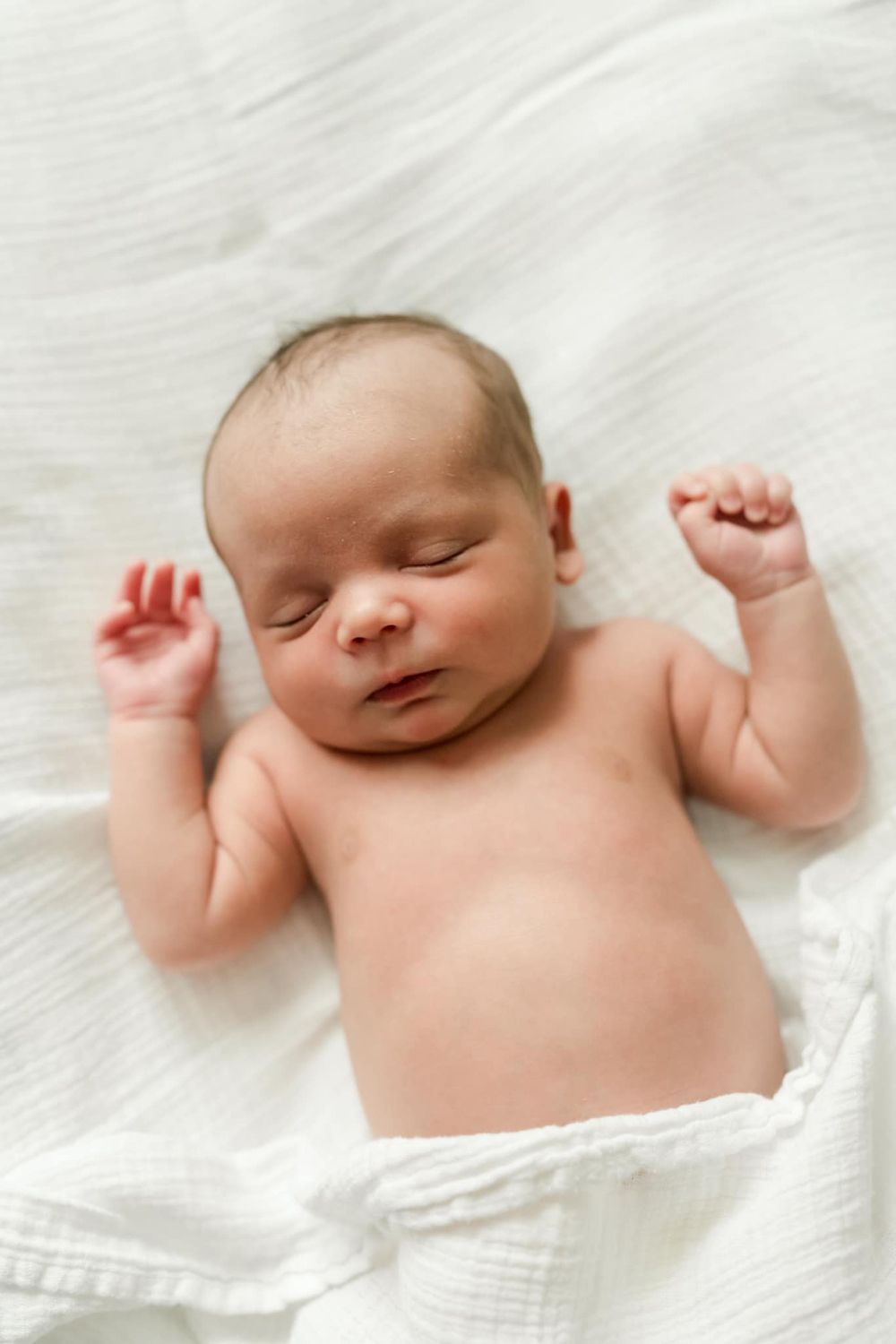 Sleeping newborn baby lying on white blanket with arms raised.
