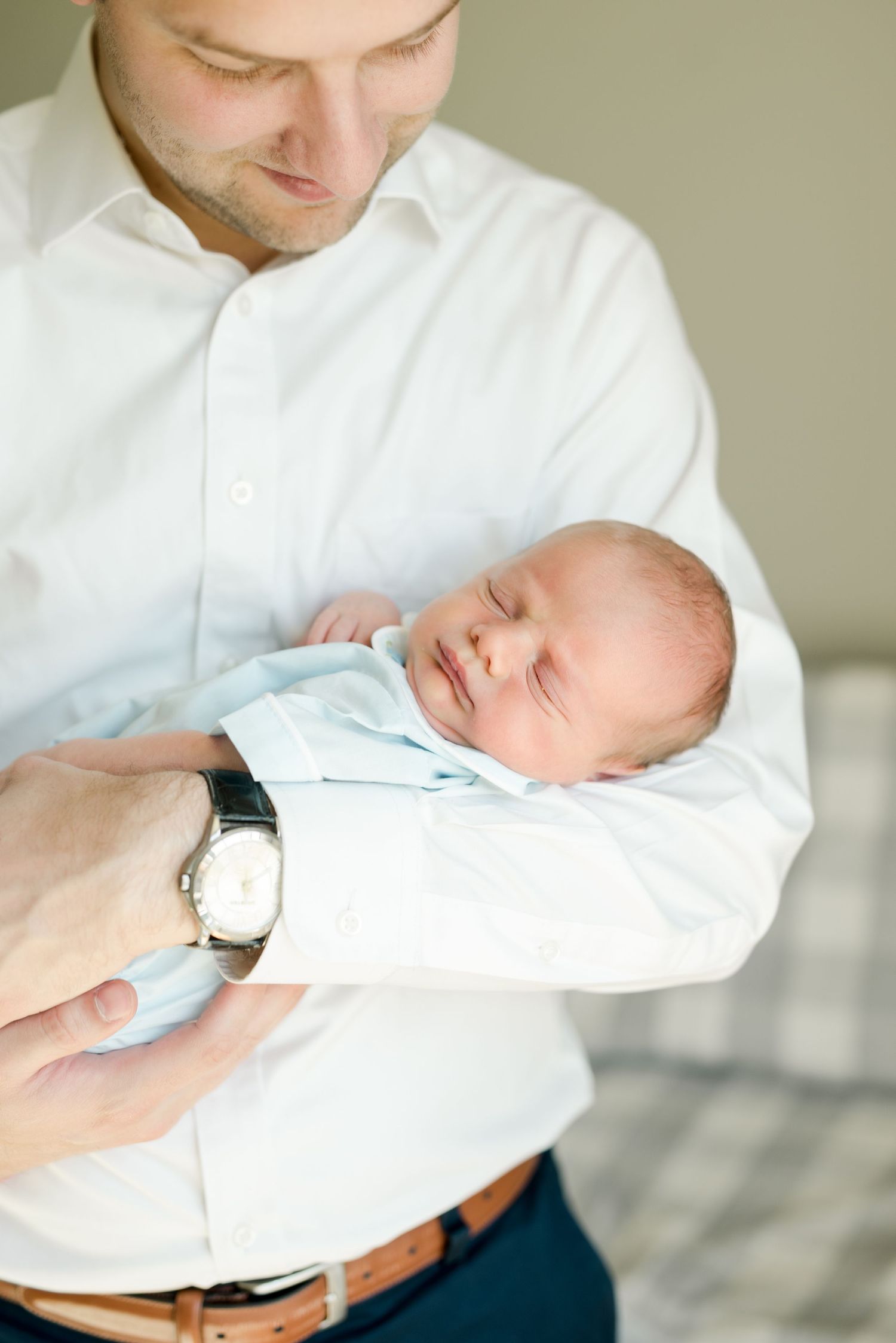 Tender moment of father in white shirt holding sleeping newborn baby.