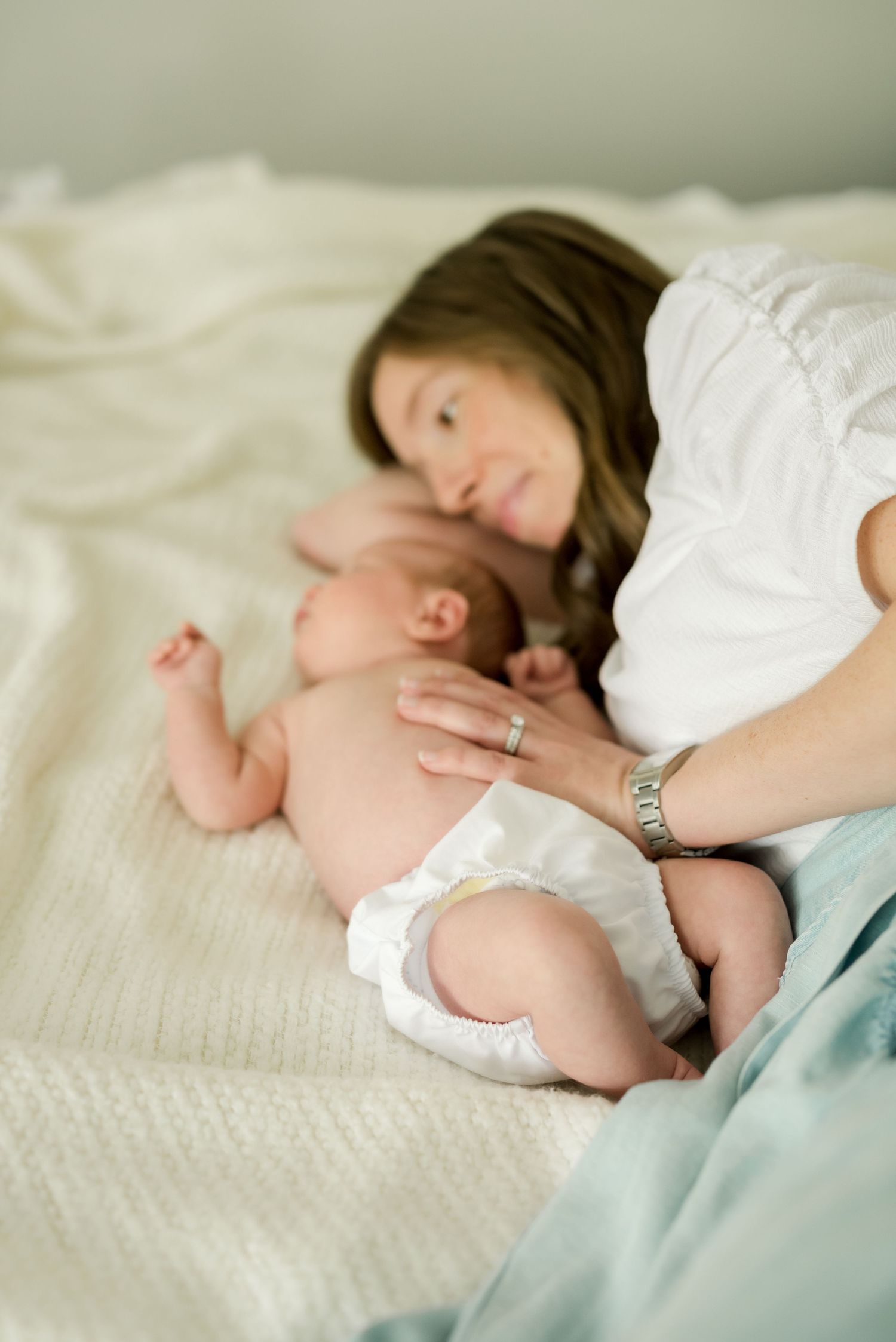 Intimate moment on white bedding as they bond with a newborn baby wearing a diaper.