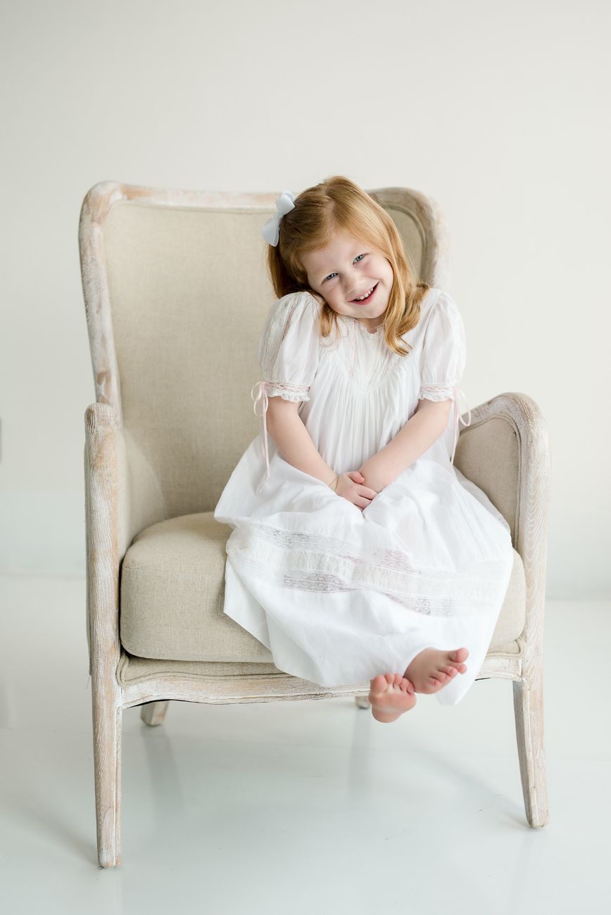 A candid moment of laughter captured in a white dress against a minimalist background.