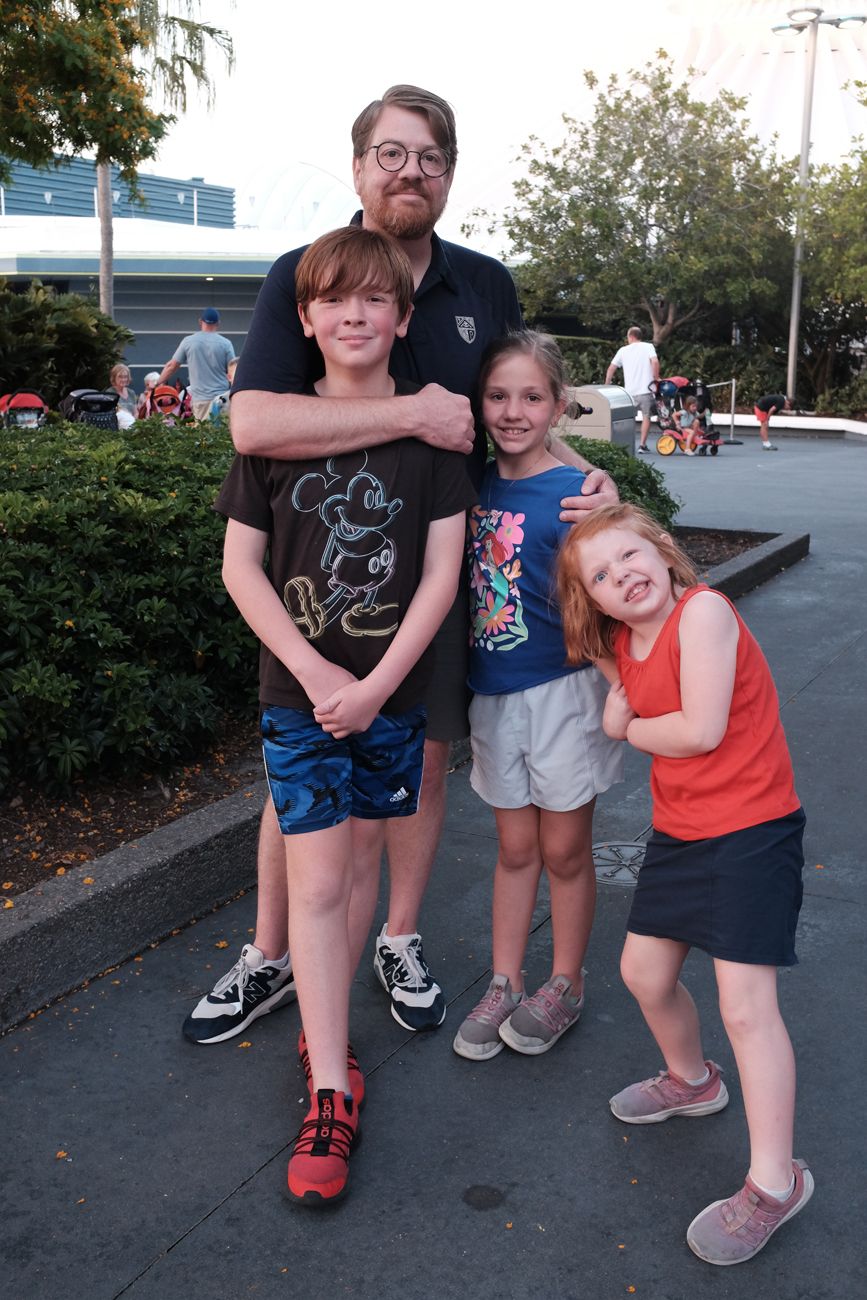 A group poses together outdoors near some landscaping at a theme park.