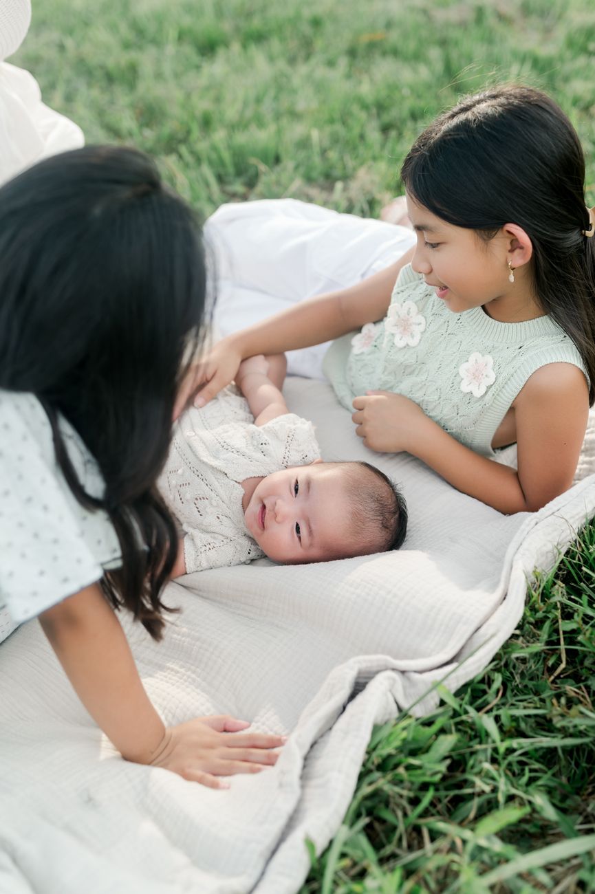 Baby lying on blanket outdoors while being tenderly cared for on a sunny day.