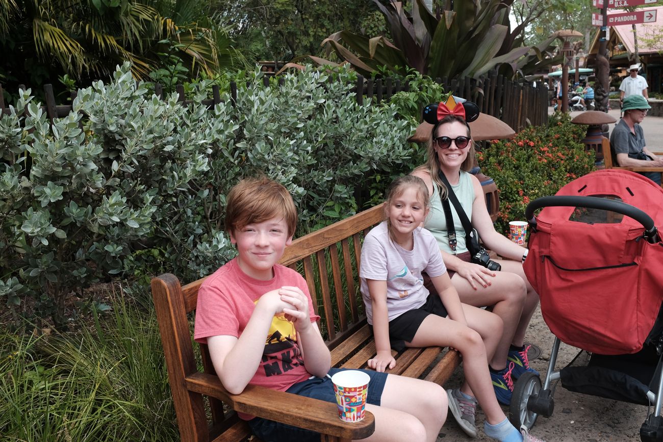 People sitting on a wooden bench enjoying refreshments in a garden setting.