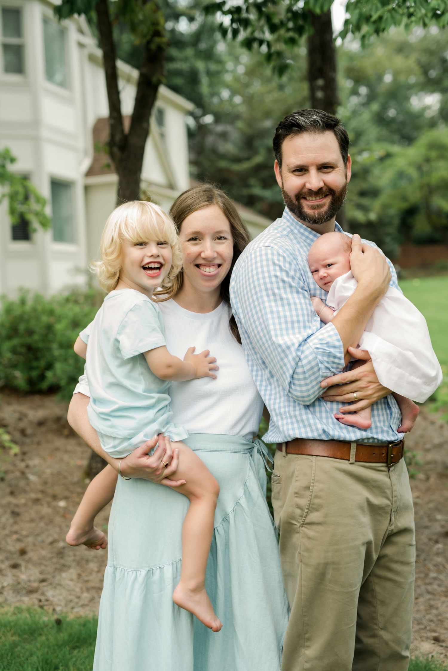 Happy family of four posing outdoors in coordinated white and blue outfits.