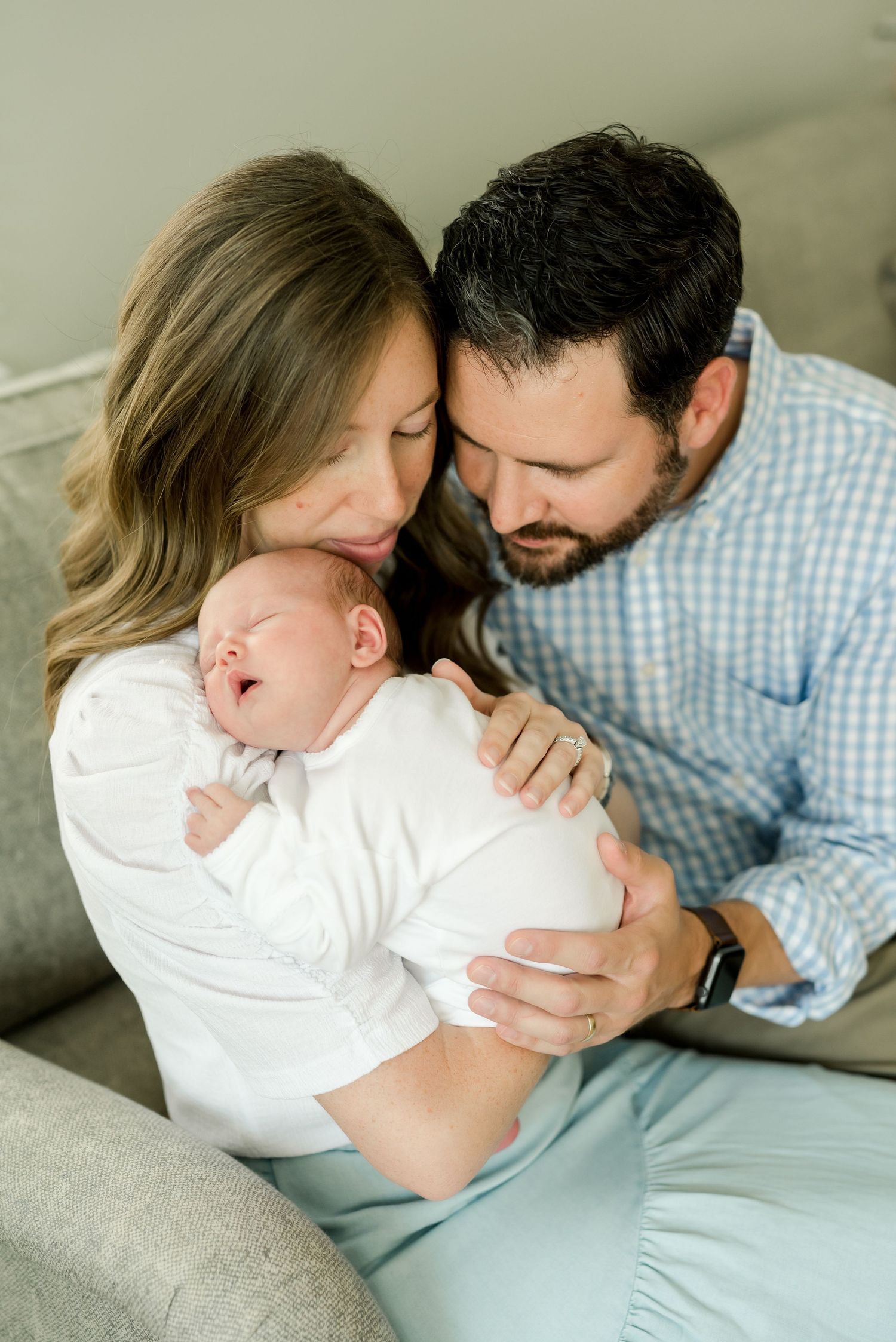 Intimate family moment with newborn baby on grey couch.