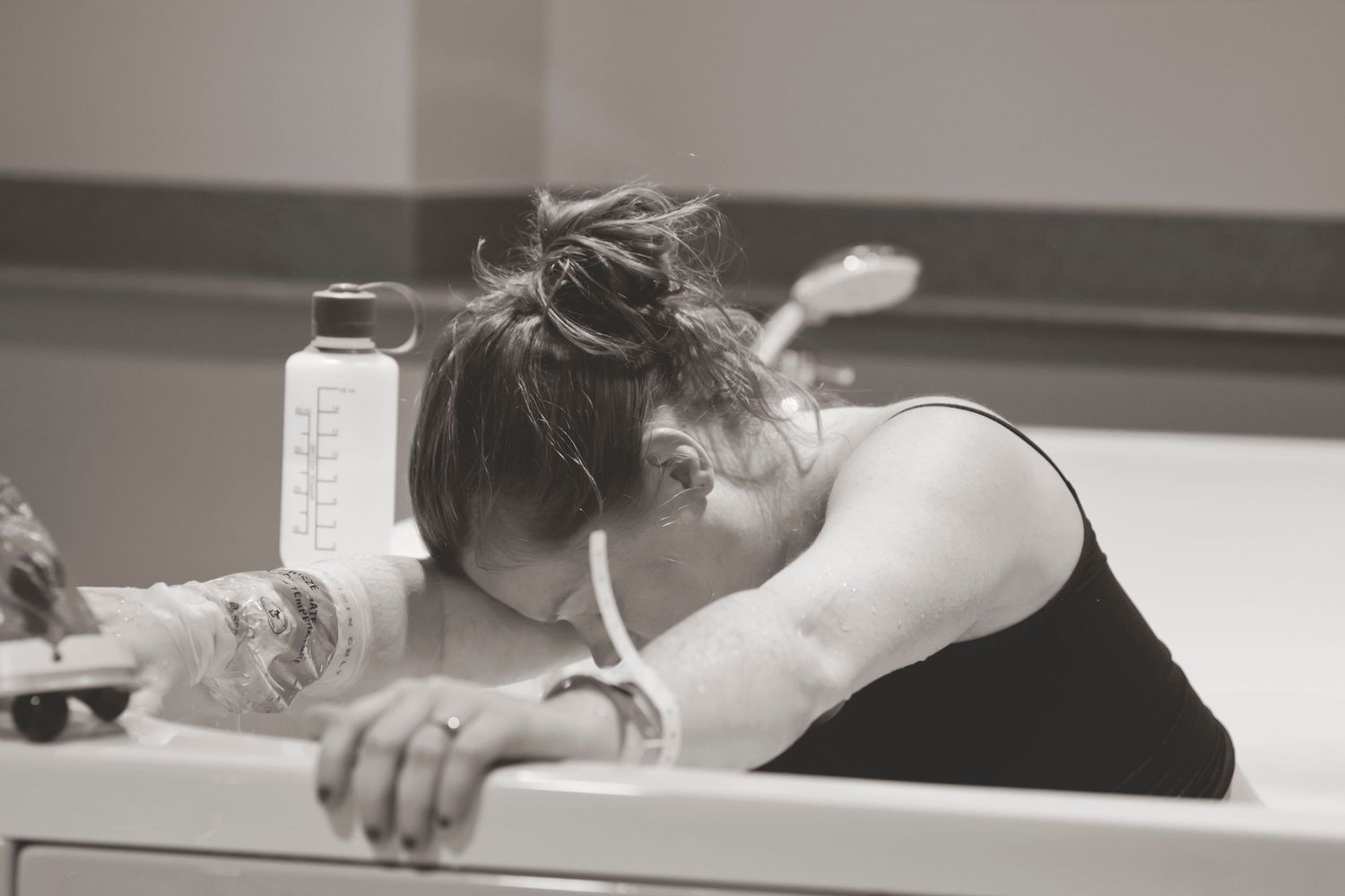 Black and white image of exhausted person resting head on bathroom counter.