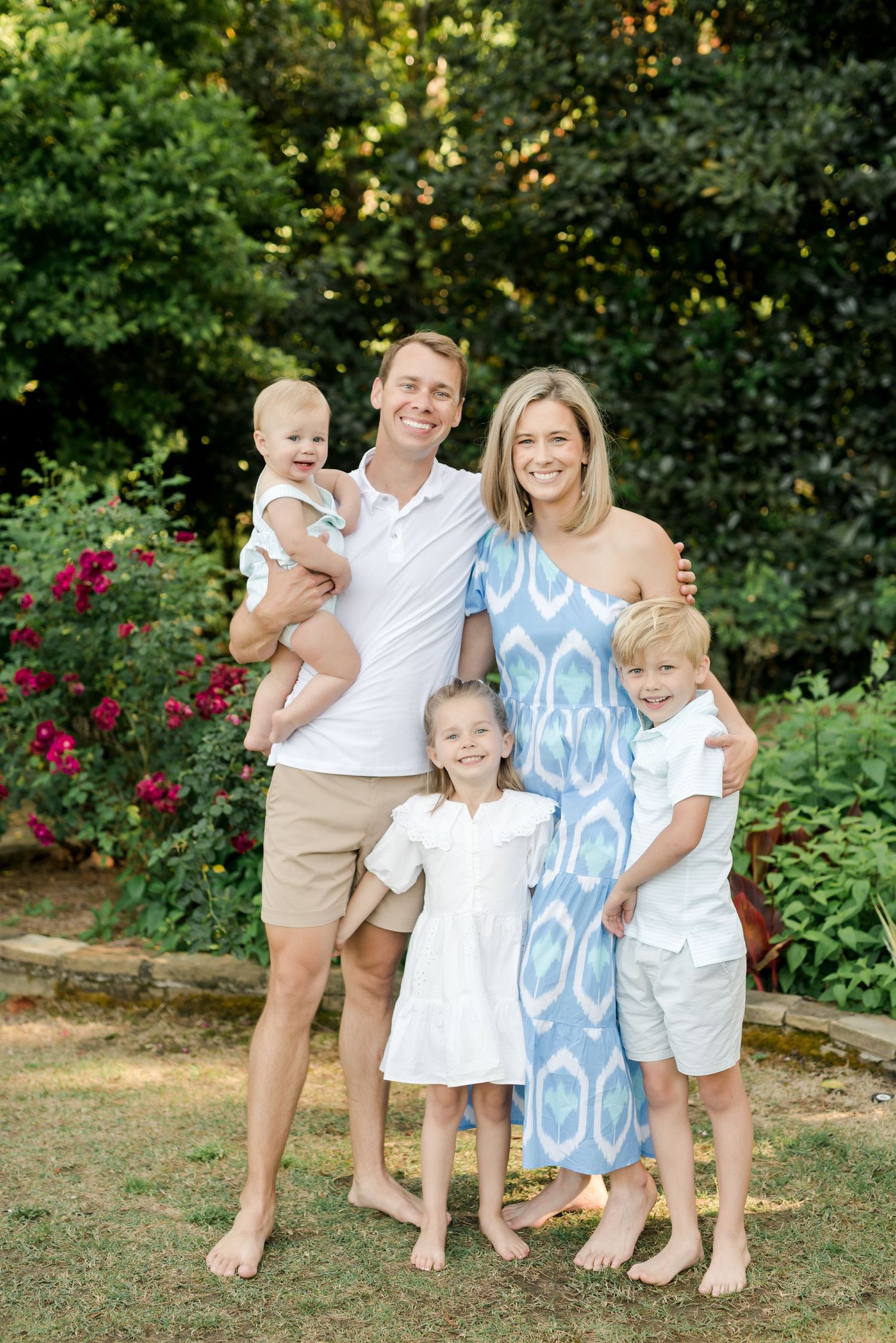 Family of five in coordinated white and blue outfits posing together in a garden setting.