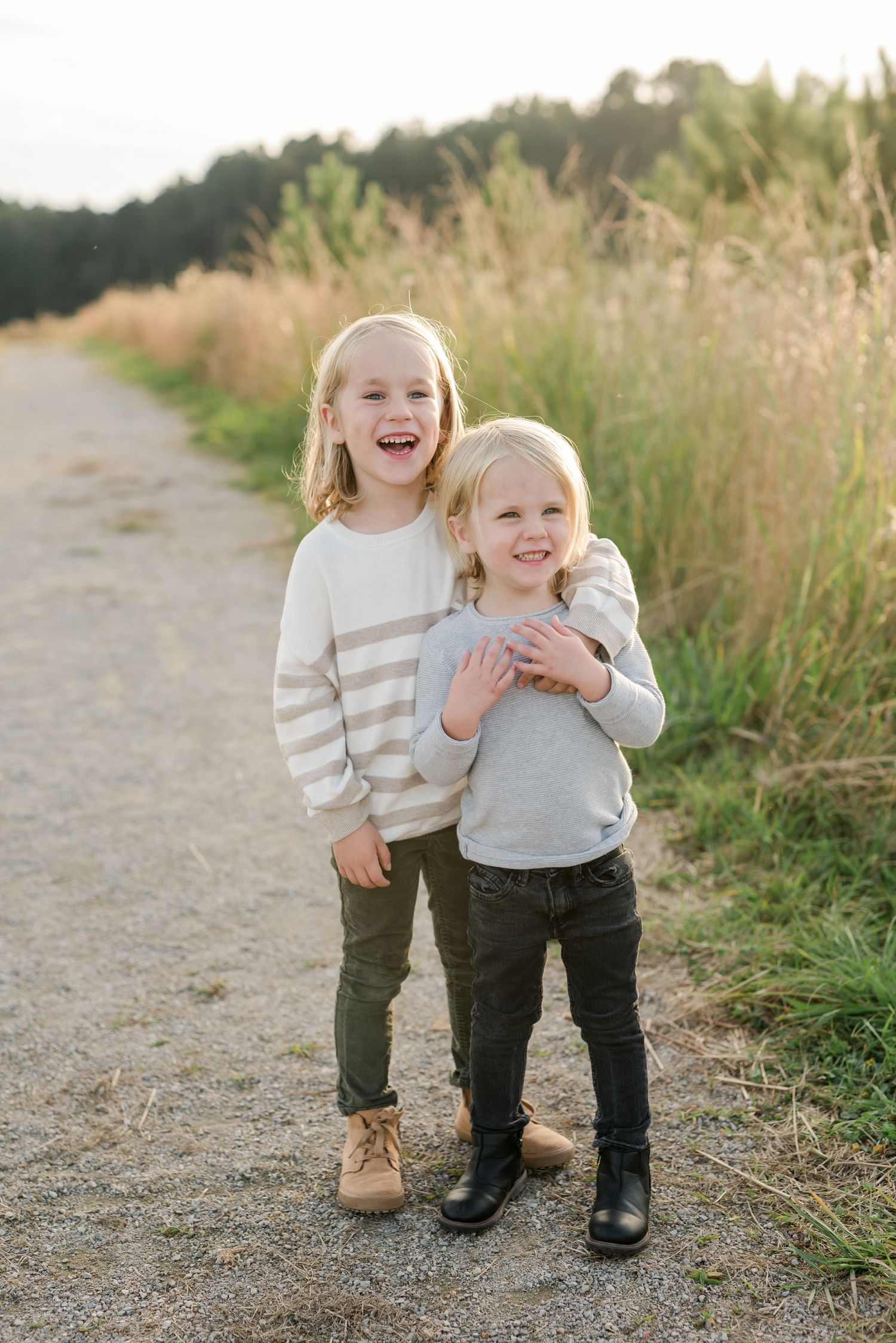 Two children laughing together on a country path surrounded by tall grasses.