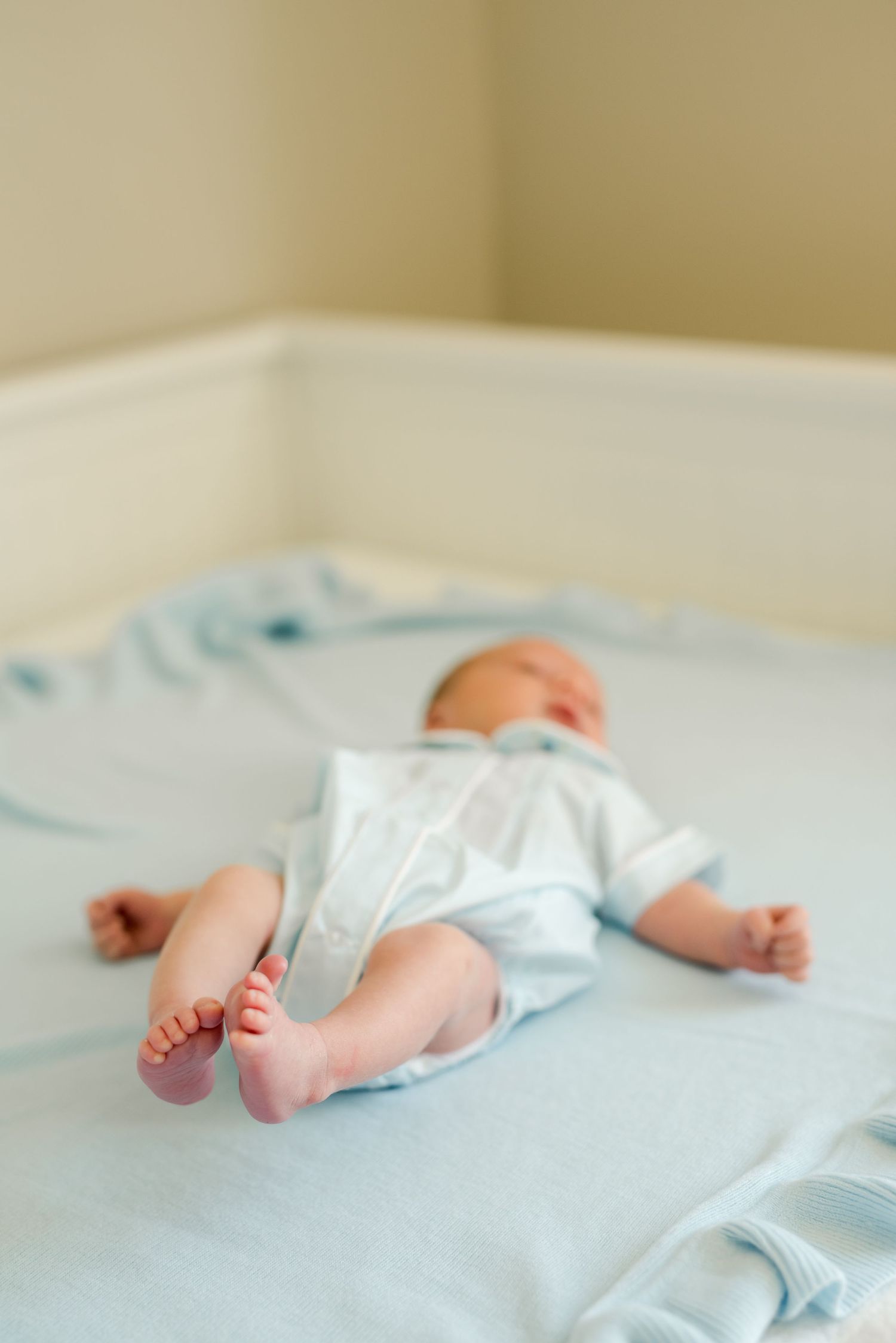 Sleeping newborn baby in light blue outfit lying on white bedding.