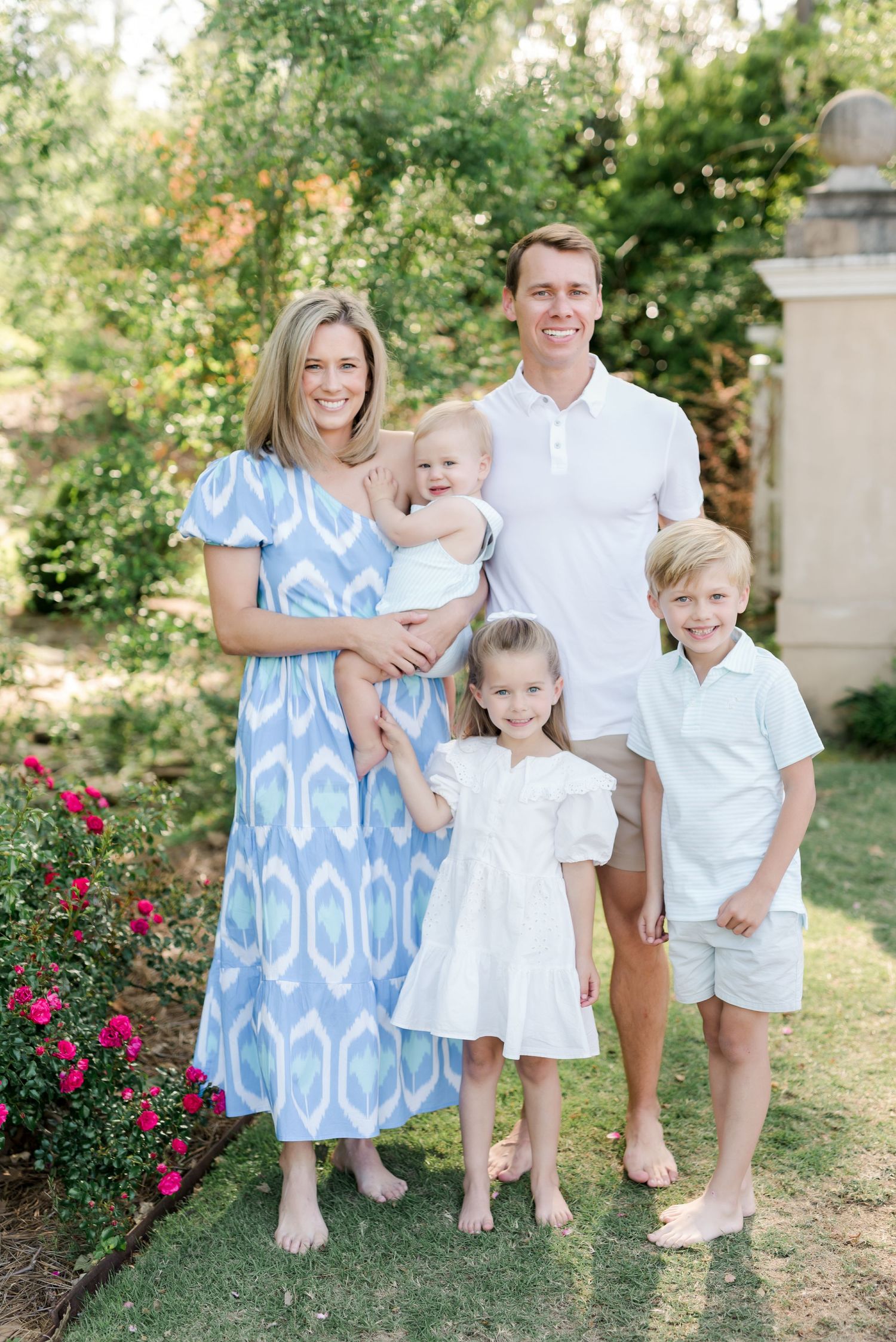 Family poses together in matching summer outfits in front of a garden with blooming flowers.