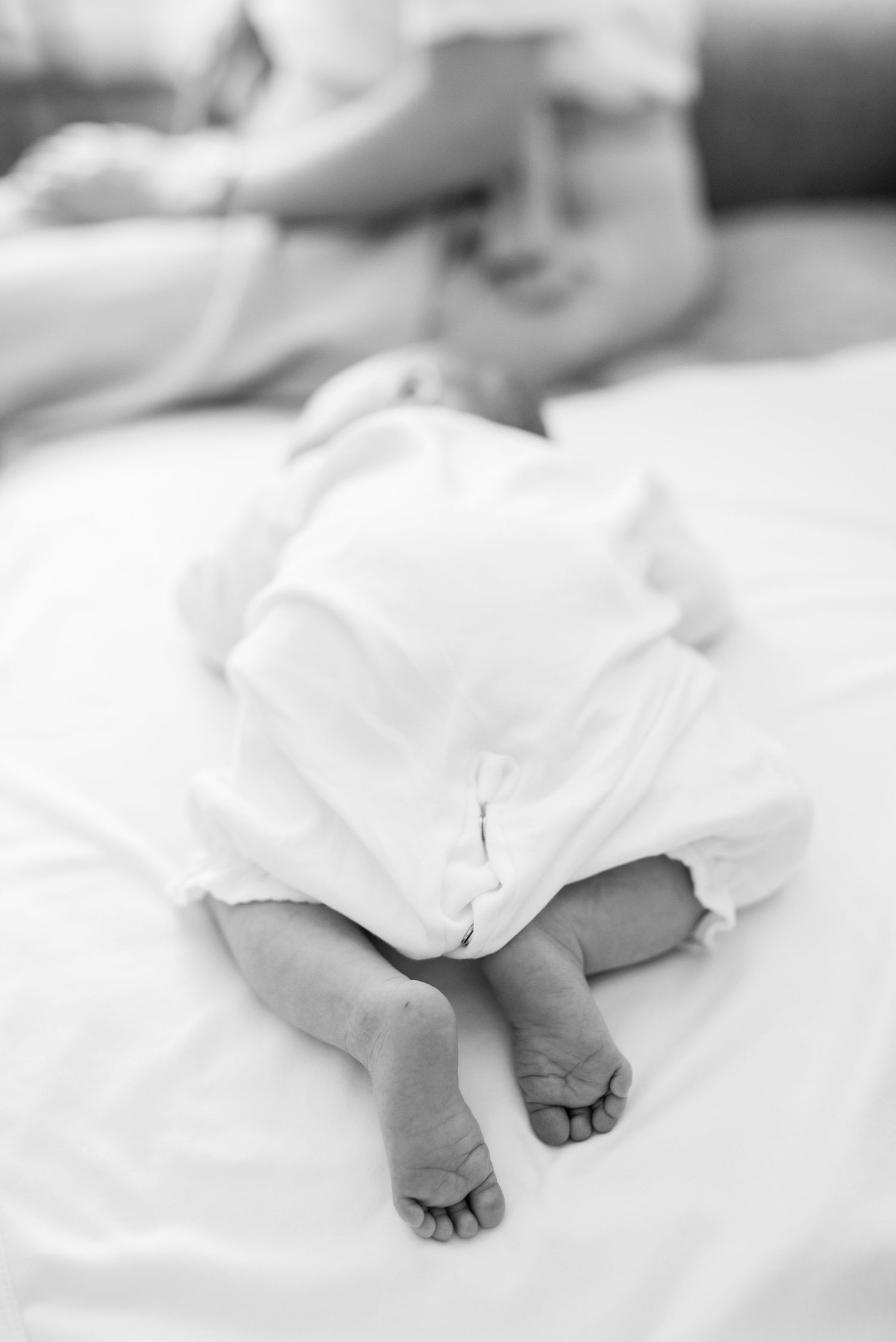 Black and white image of tiny feet peeking out from white fabric on bed.