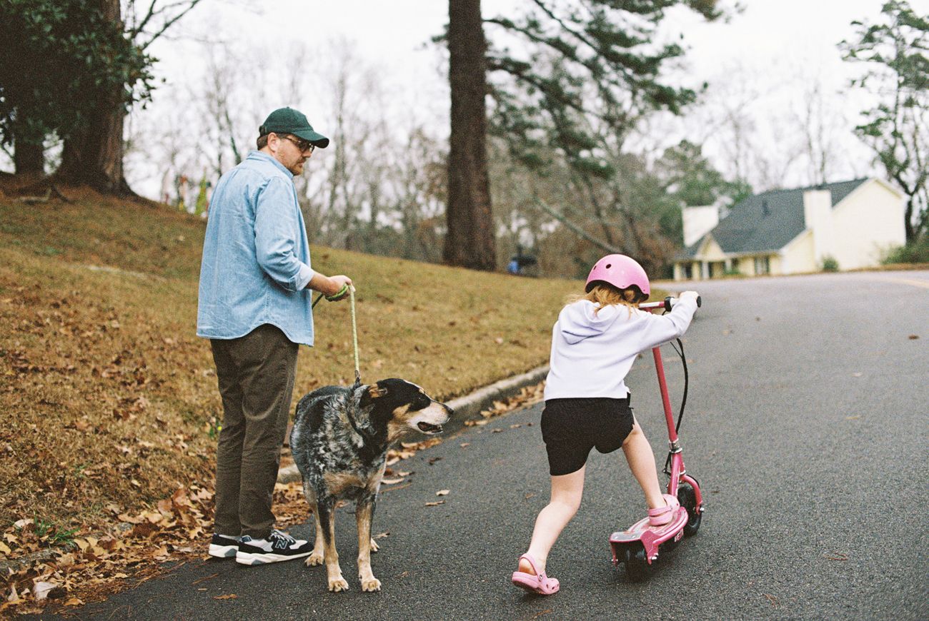 People walking with children and strollers on an autumn path covered in fallen leaves.