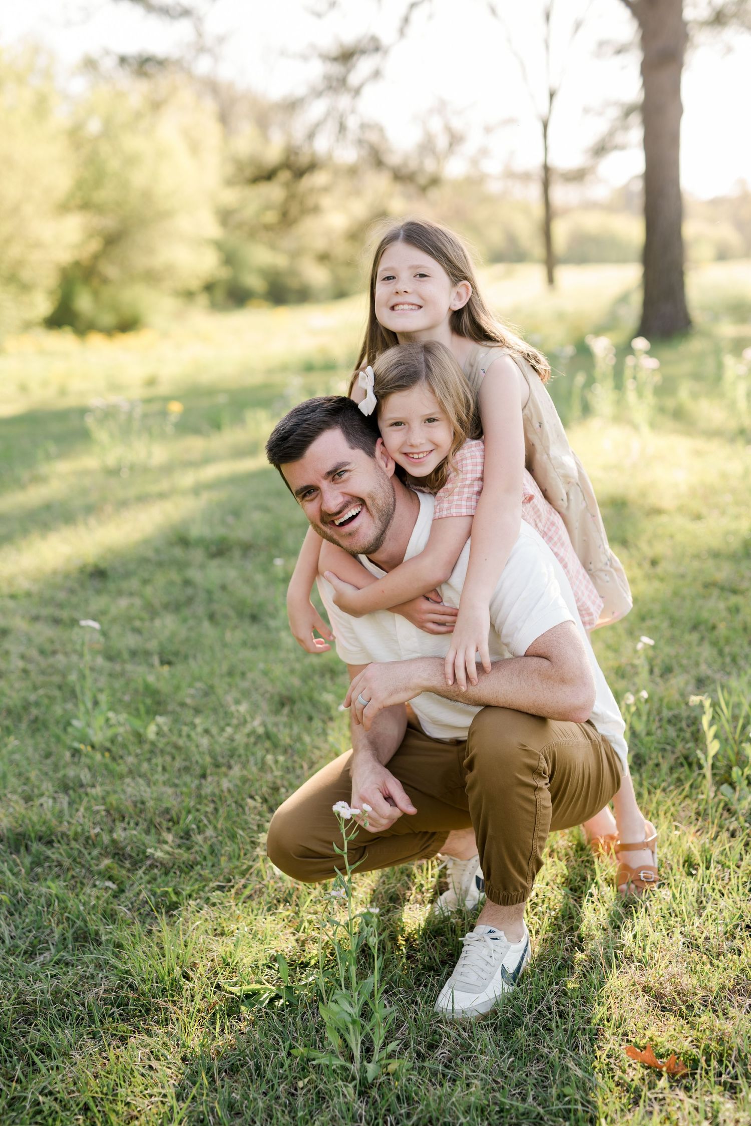 Playful family moment captured as children climb on parent's shoulders in golden evening light.