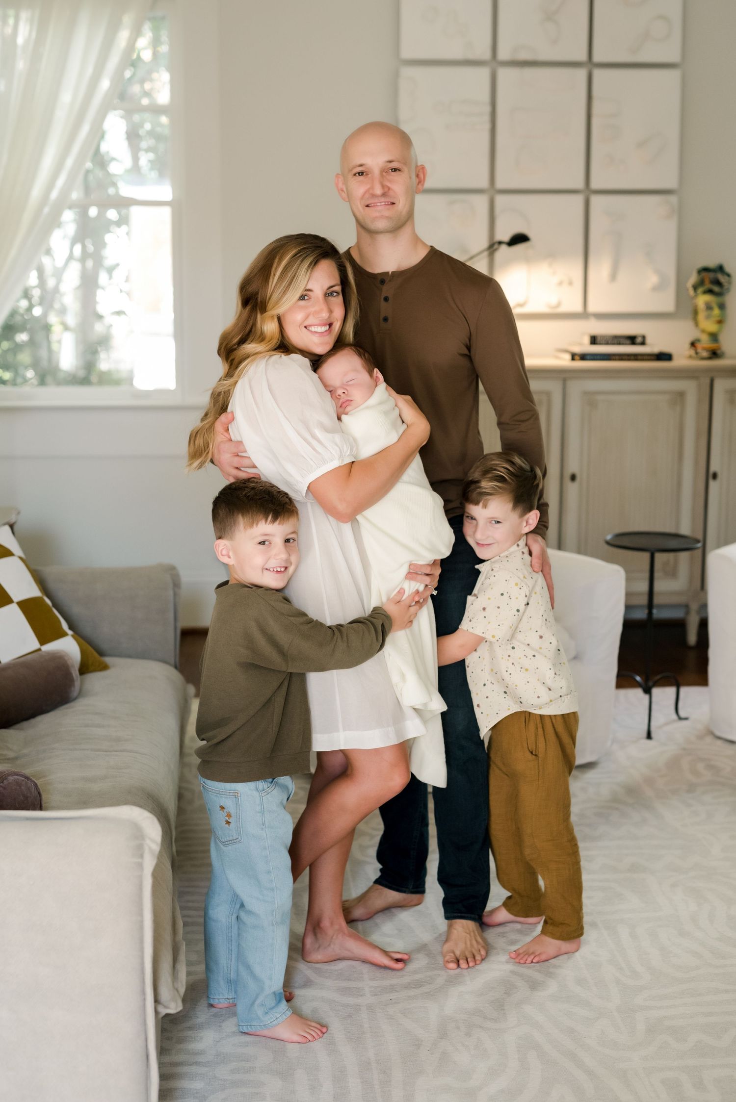 Family of five poses together in bright modern living room with wall art.