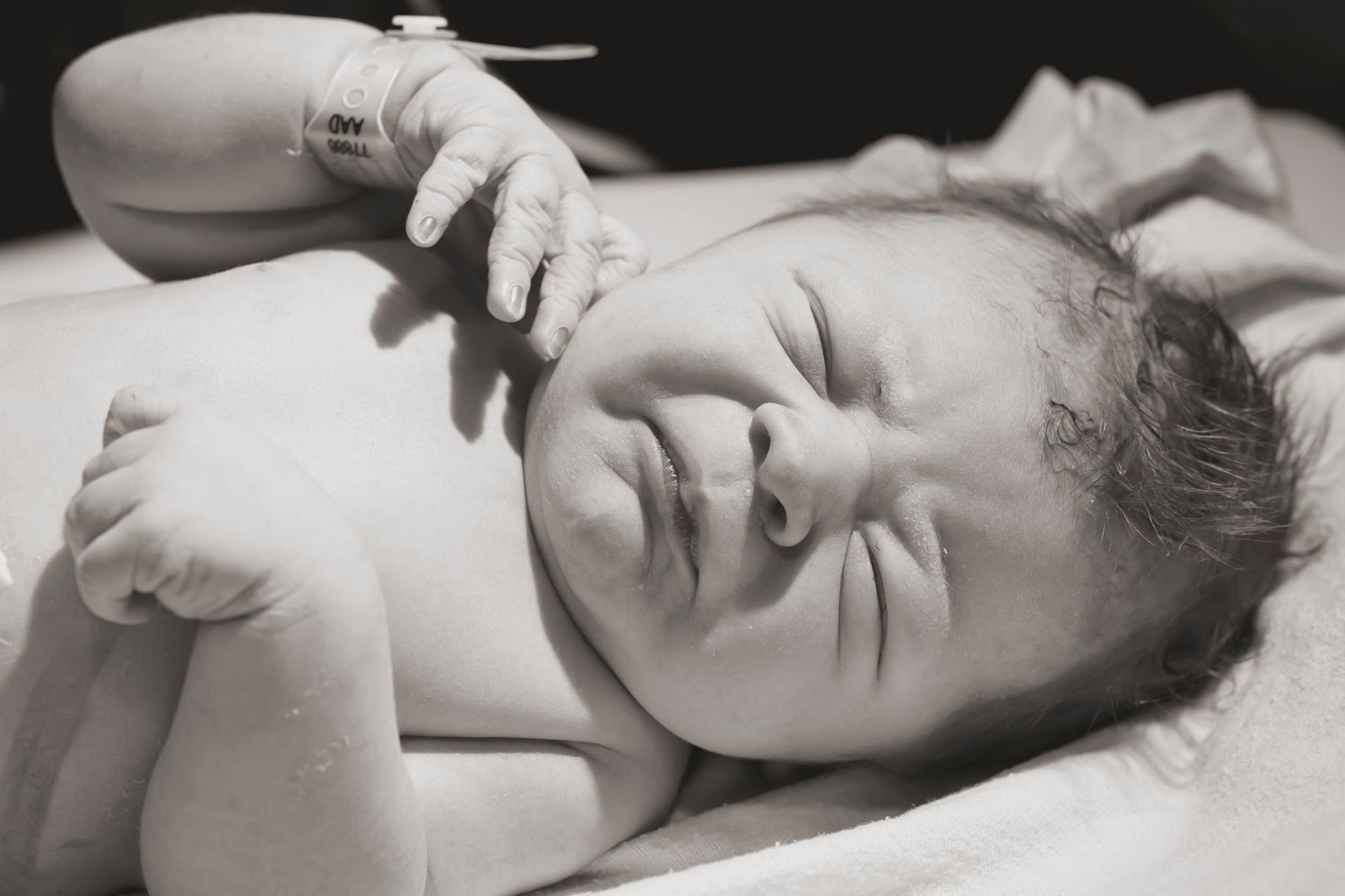 Close-up black and white portrait of a newborn baby lying on hospital bed.