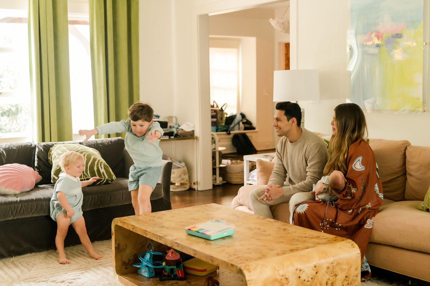 Family relaxing in a cozy living room with two young children playing near a wooden coffee table.