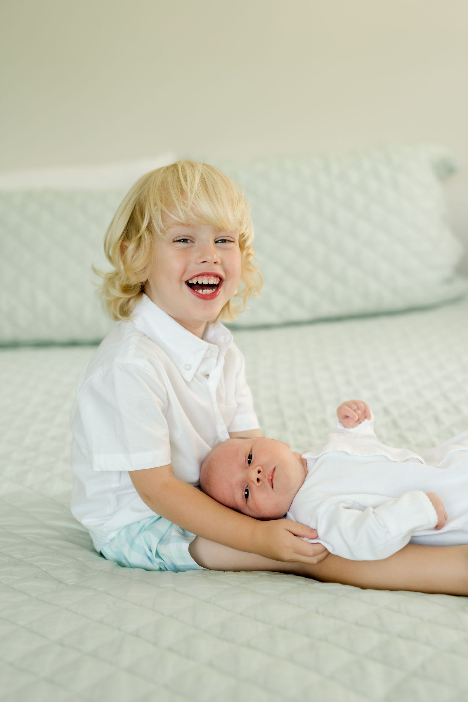 Two siblings share a tender moment on mint green bedding.