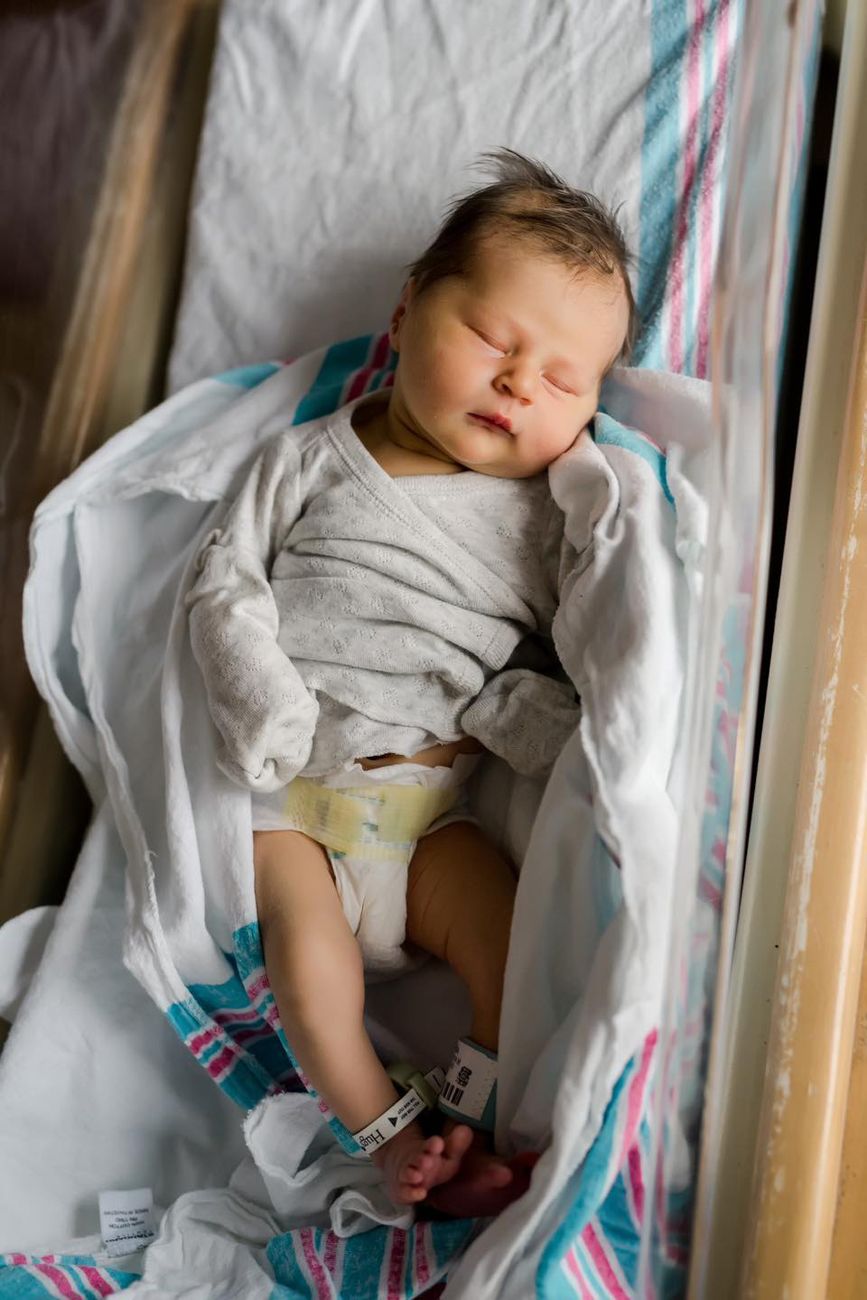 Sleeping infant in white onesie resting peacefully in crib with striped blanket.
