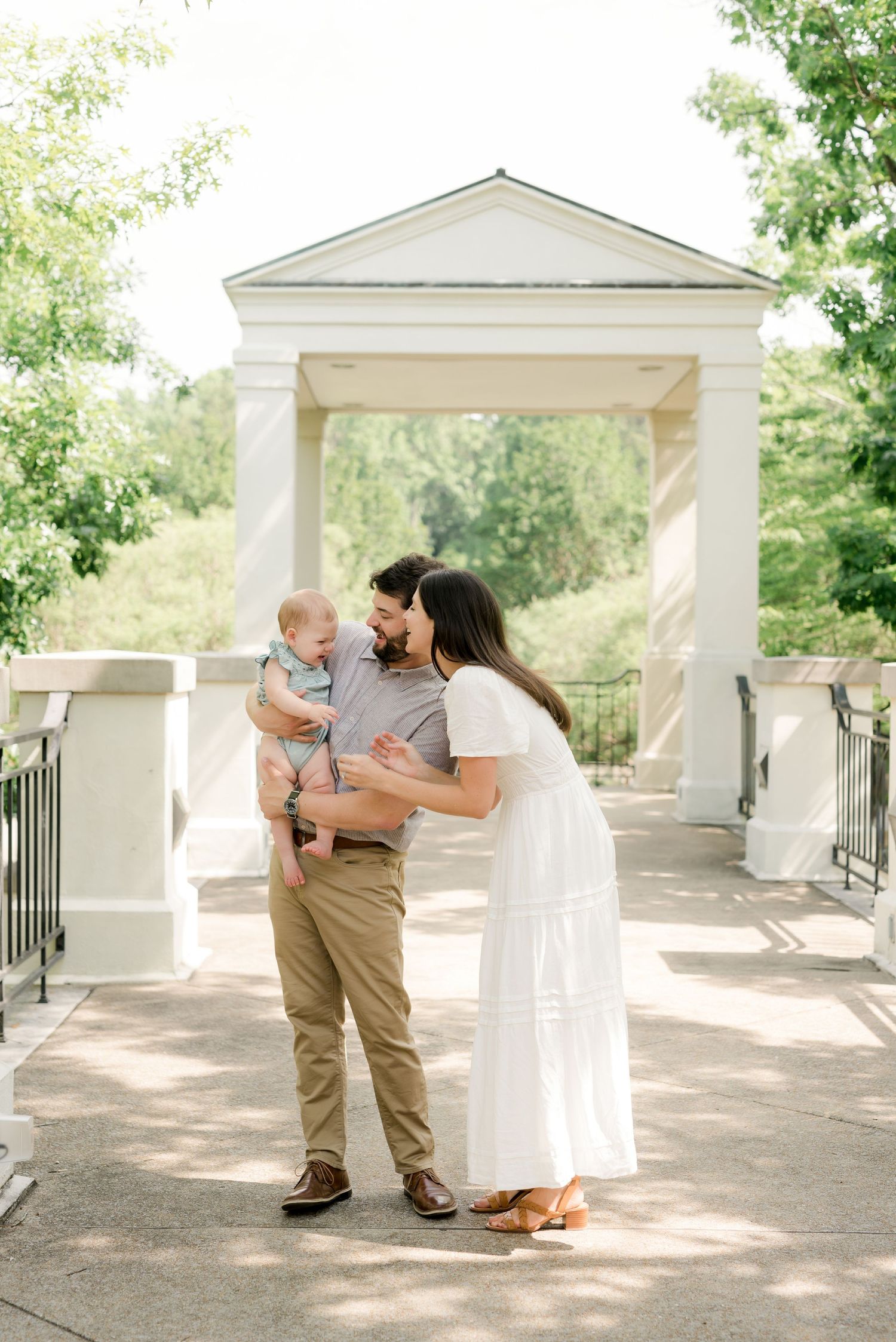 Family portrait on white columned porch surrounded by lush greenery.