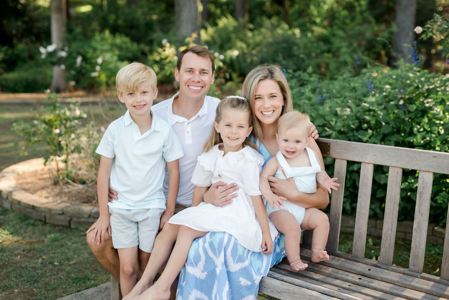 Family in coordinated outfits sitting together on wooden garden bench.