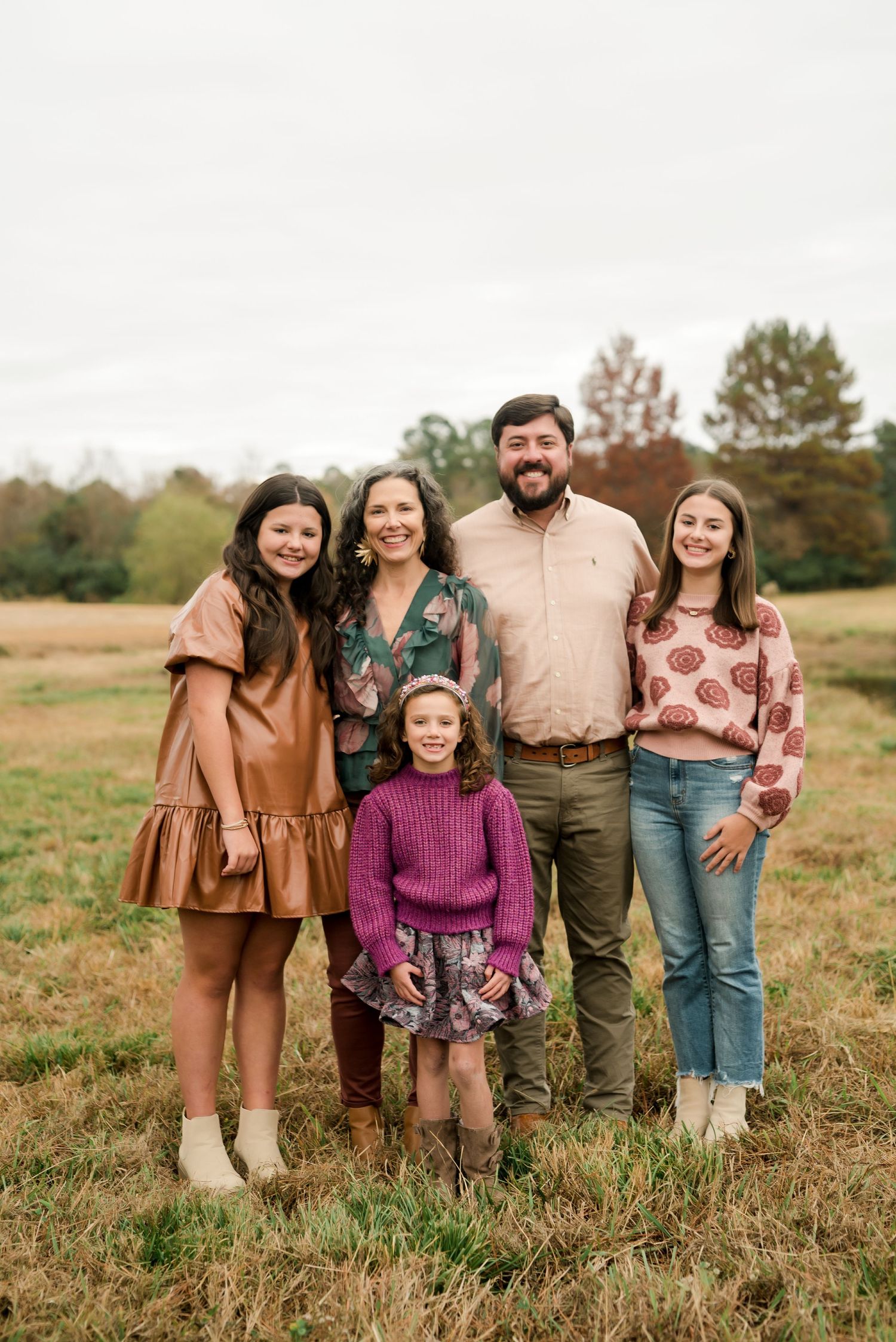 Family of five in coordinated fall outfits standing together in grassy field.